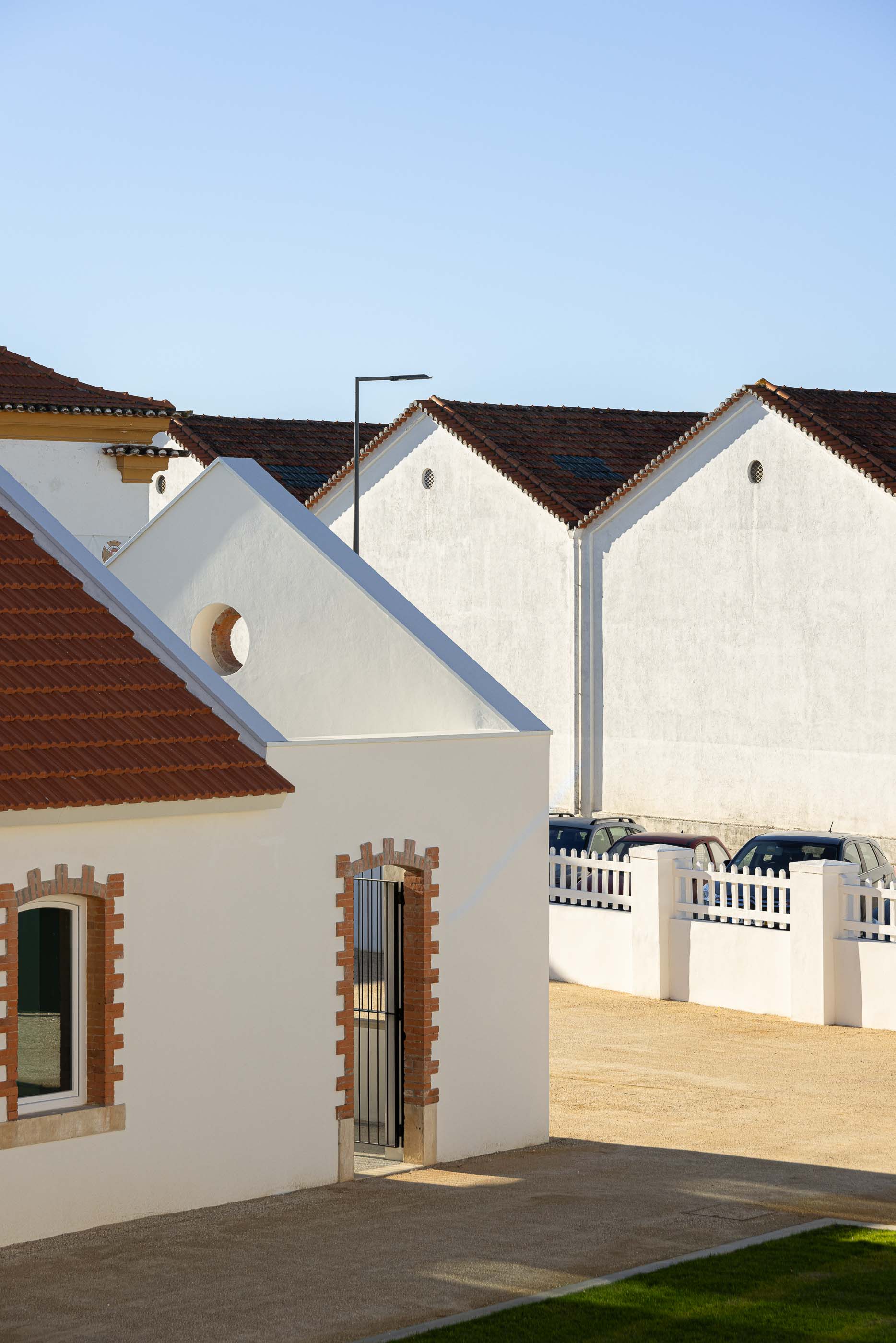 Exterior: Edifícios brancos com telhado cerâmico, pátio com gravilha e vedação em madeira. — Reabilitação Urbana do Bairro do Boneco arquitetura Adarq - André David Arquitecto em Entroncamento