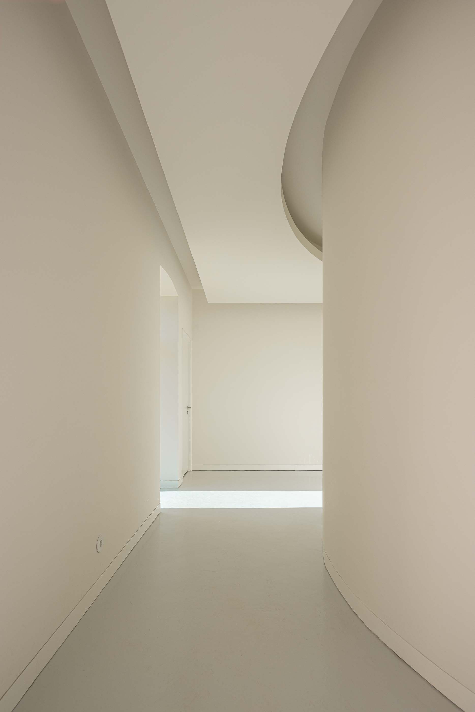 Corredor: Espaço interior com paredes curvas, pavimento claro e iluminação embutida. — Reabilitação Urbana do Bairro do Boneco arquitetura Adarq - André David Arquitecto em Entroncamento