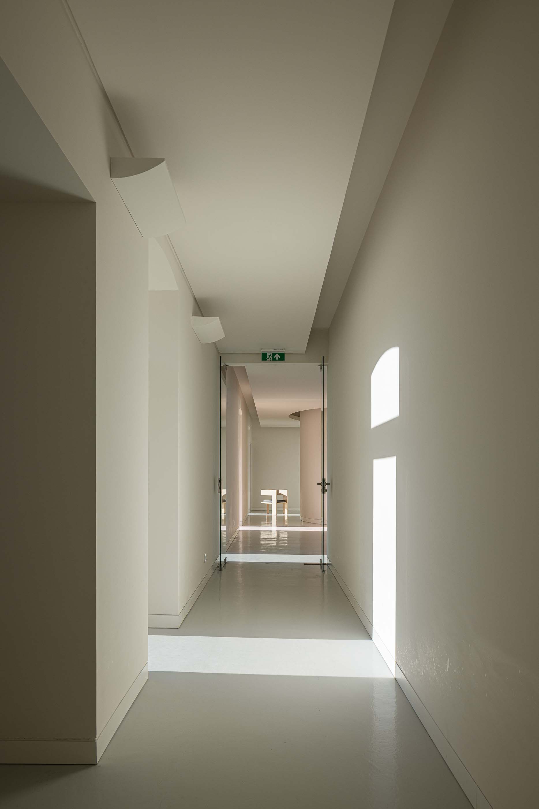Corredor: Espaço interior com paredes brancas, pavimento claro e portas envidraçadas. — Reabilitação Urbana do Bairro do Boneco arquitetura Adarq - André David Arquitecto em Entroncamento
