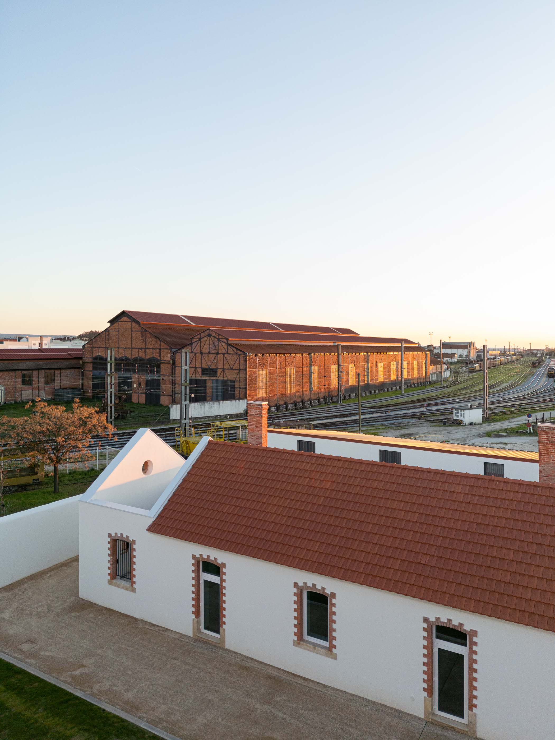 Vista exterior: Edifícios brancos com telhado cerâmico, armazéns ferroviários em tijolo e linhas de comboio. — Reabilitação Urbana do Bairro do Boneco arquitetura Adarq - André David Arquitecto em Entroncamento