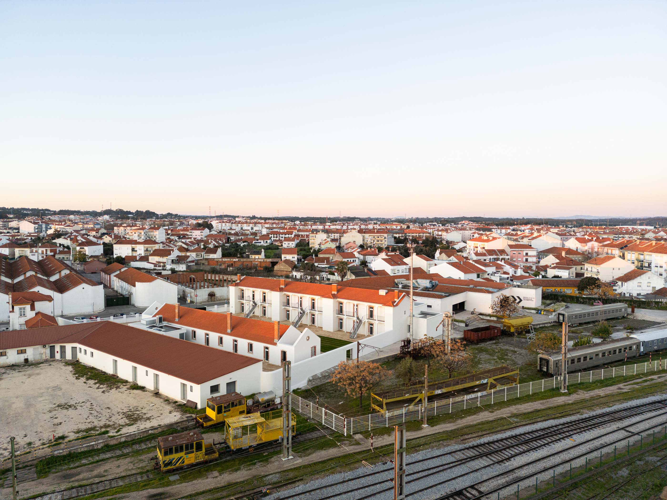 Vista aérea: Conjunto habitacional branco com telhados vermelhos, integrado na malha urbana e zona ferroviária. — Reabilitação Urbana do Bairro do Boneco arquitetura Adarq - André David Arquitecto em Entroncamento