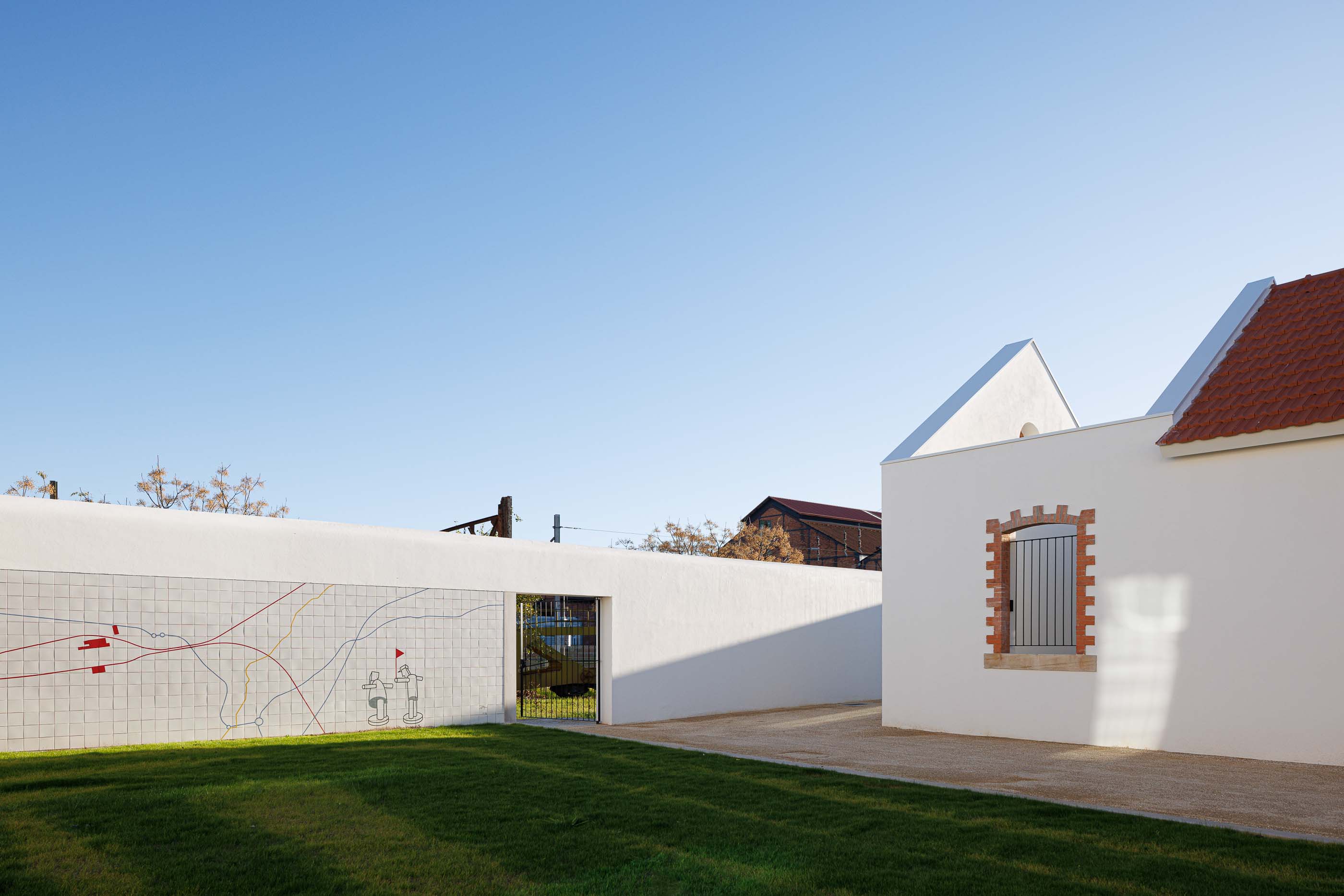 Exterior: Muro com revestimento cerâmico e desenho linear a cores, com portão de acesso ao pátio. — Reabilitação Urbana do Bairro do Boneco arquitetura Adarq - André David Arquitecto em Entroncamento
