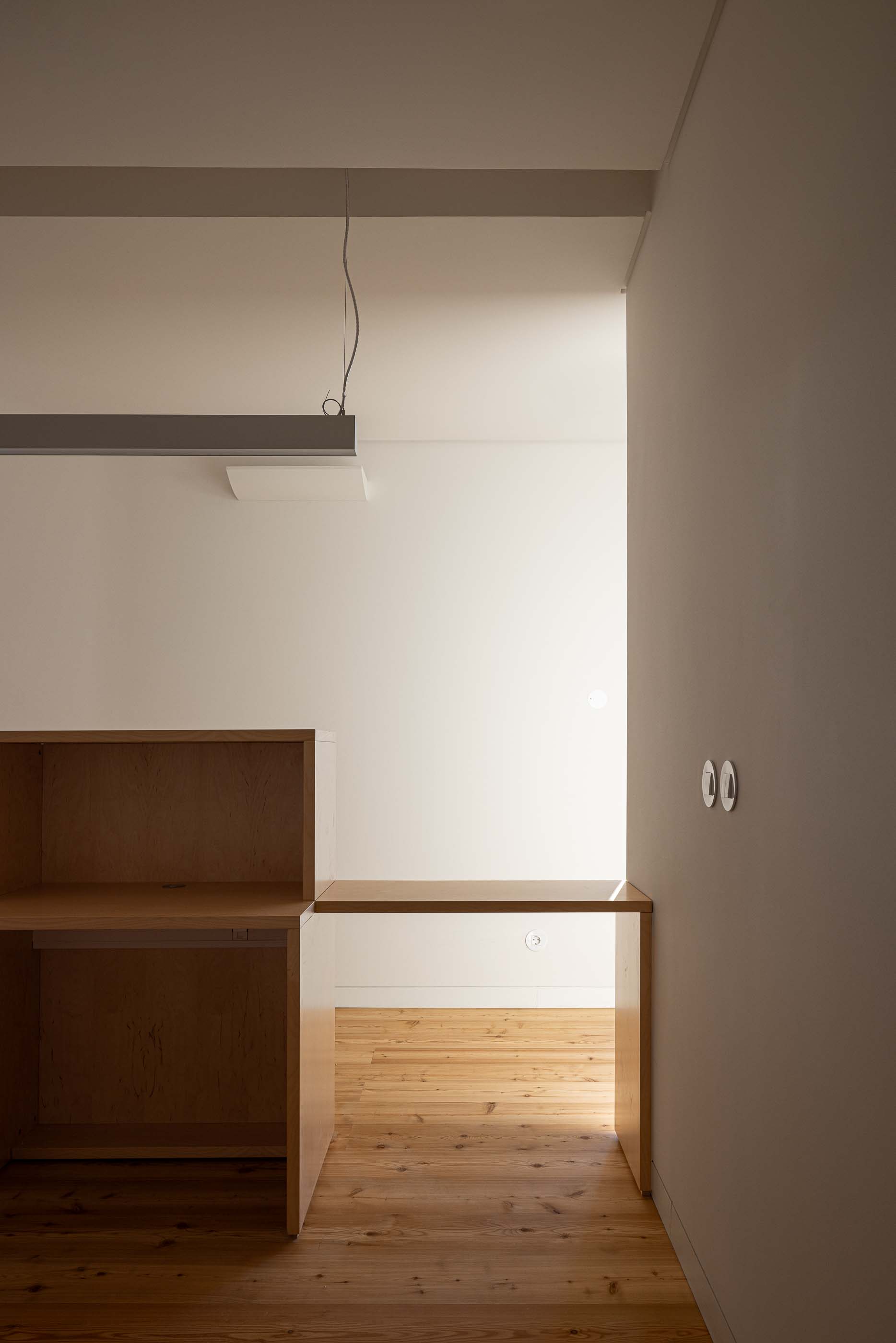 Espaço amplo: Balcão em madeira clara, pavimento em madeira e iluminação linear suspensa. — Reabilitação Urbana do Bairro do Boneco arquitetura Adarq - André David Arquitecto em Entroncamento
