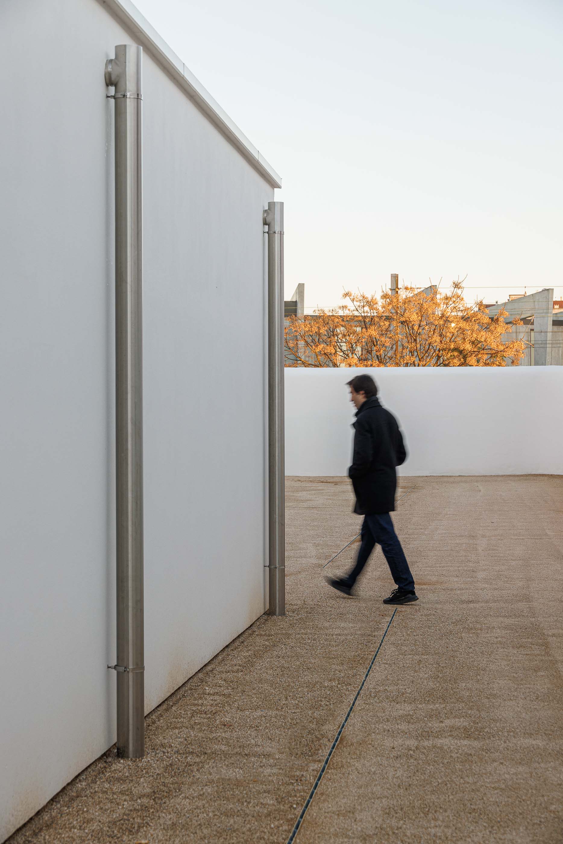Exterior: Corredor exterior com pavimento em gravilha e paredes brancas. — Reabilitação Urbana do Bairro do Boneco arquitetura Adarq - André David Arquitecto em Entroncamento