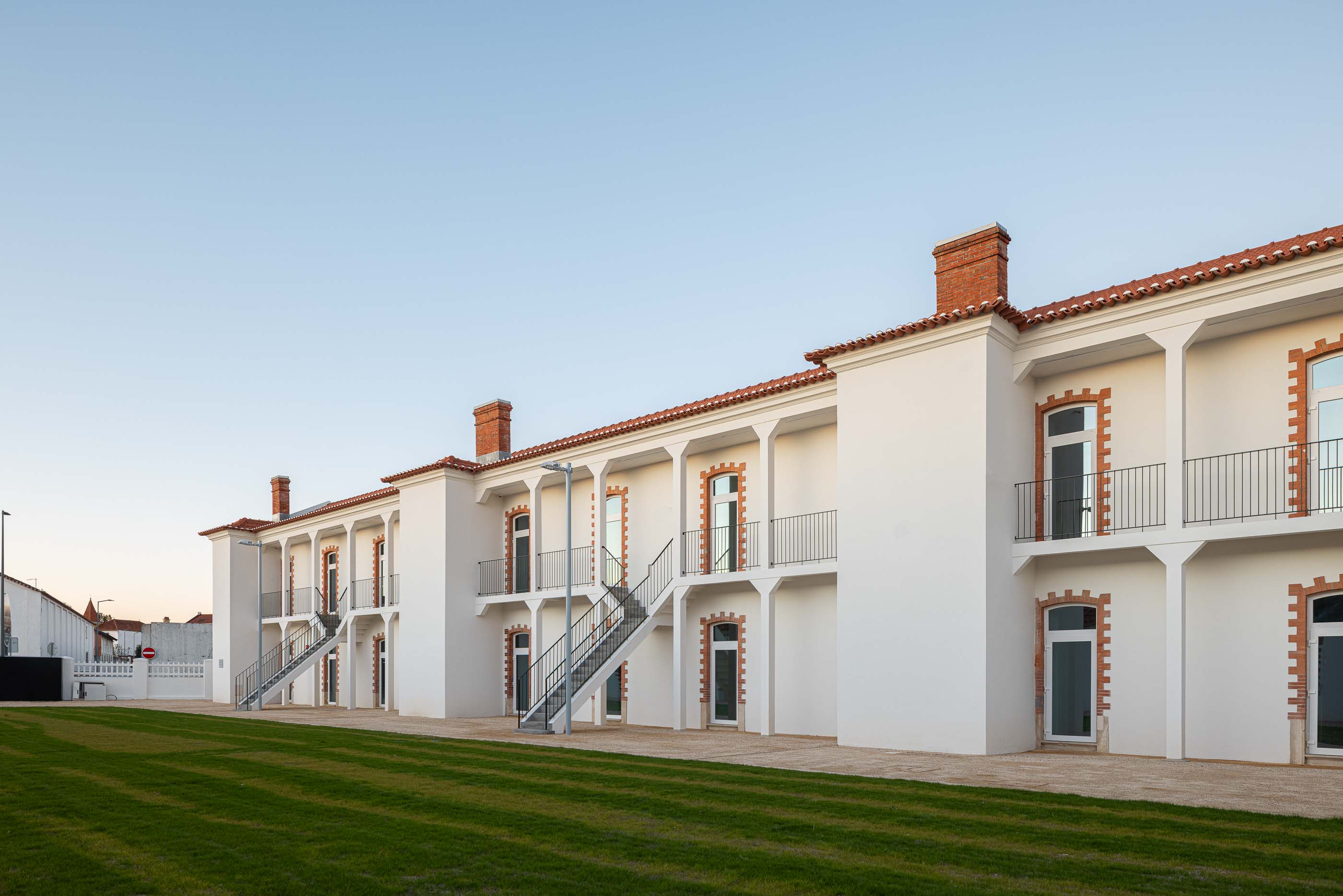 Exterior: Edifício branco com colunas, varandas em ferro e escadas de acesso aos pisos superiores. — Reabilitação Urbana do Bairro do Boneco arquitetura Adarq - André David Arquitecto em Entroncamento