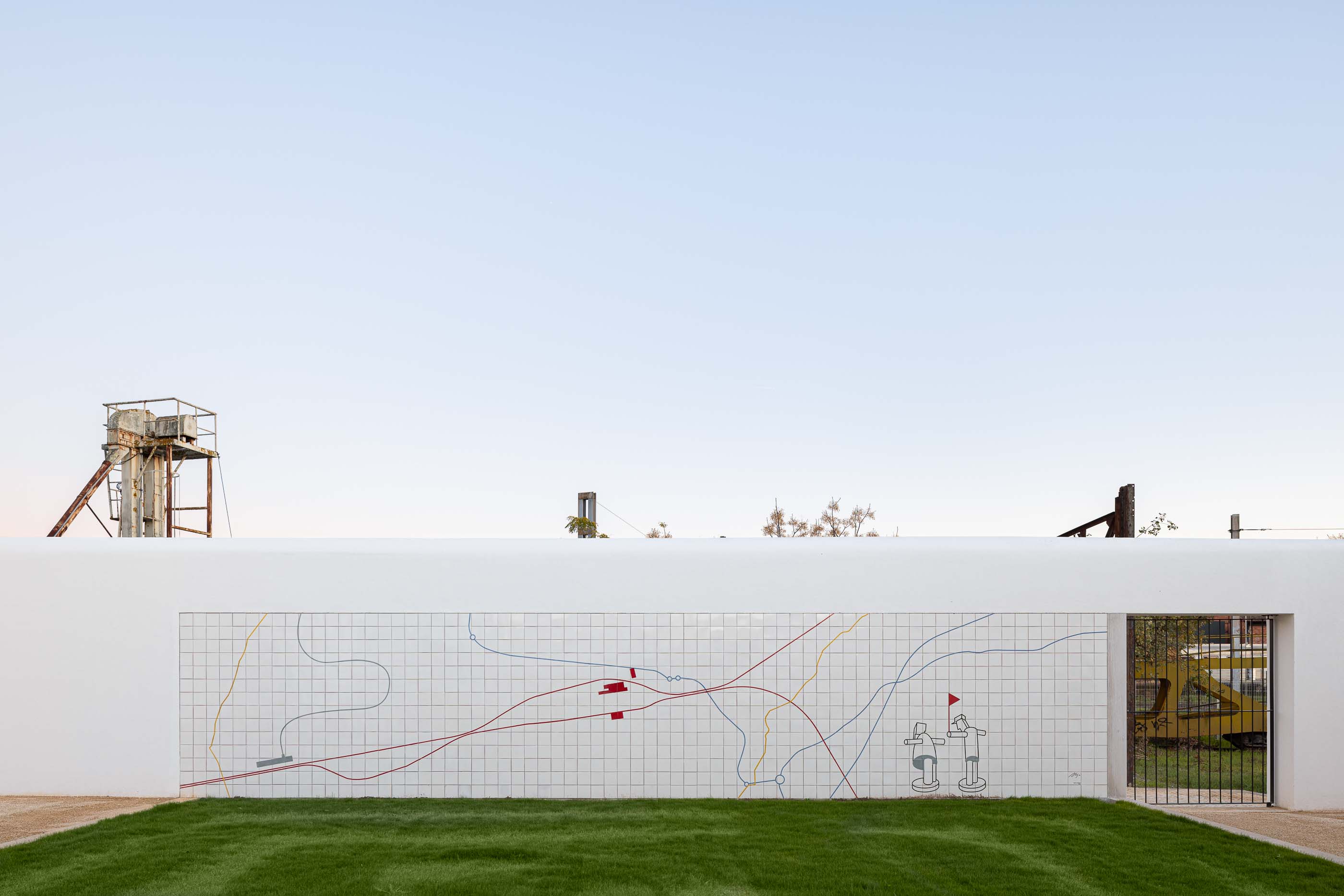 Exterior: Muro revestido com azulejos brancos e desenho linear a cores, com relvado. — Reabilitação Urbana do Bairro do Boneco arquitetura Adarq - André David Arquitecto em Entroncamento