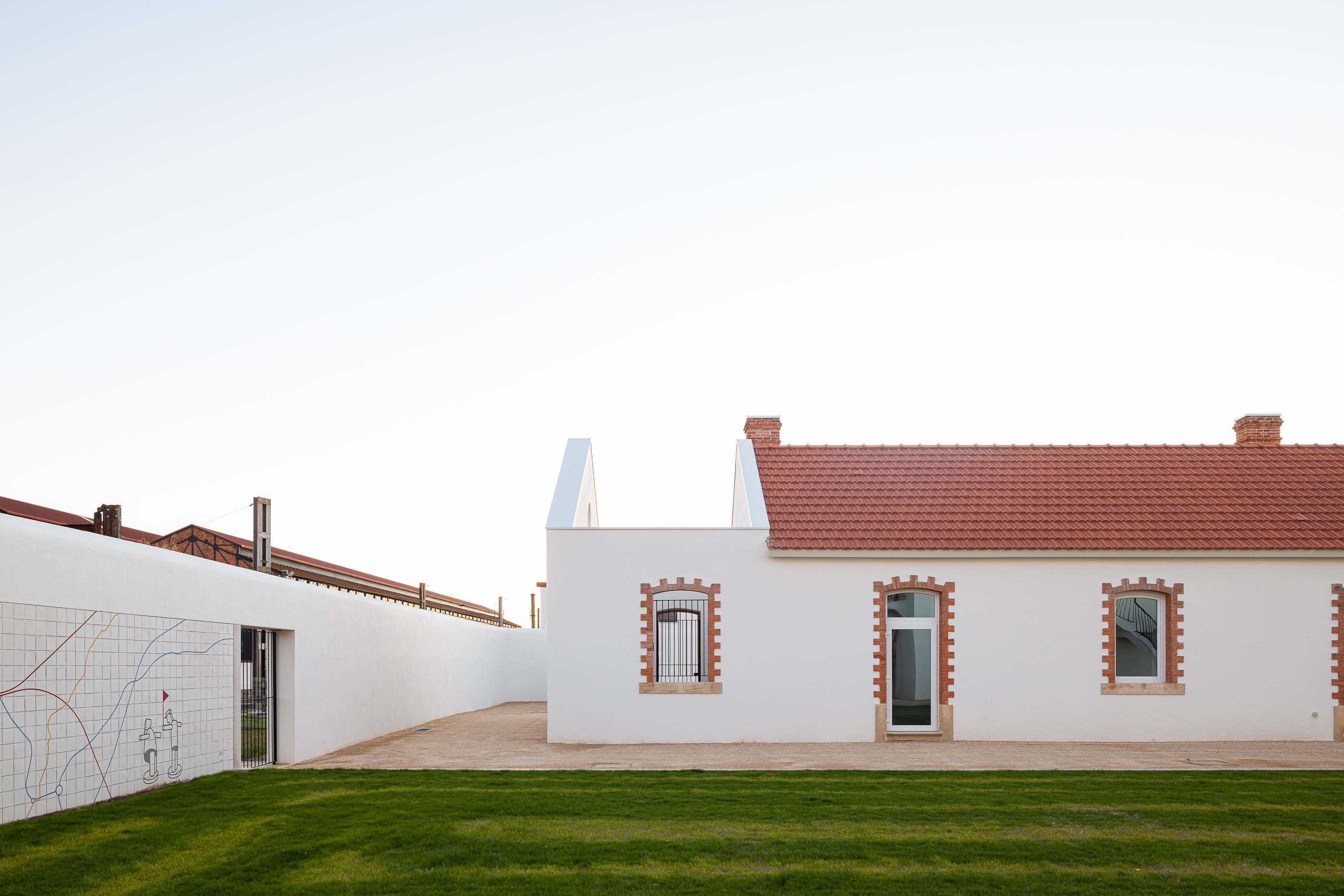 Exterior: Edifício branco com telhado cerâmico, muro com revestimento cerâmico e pátio relvado. — Reabilitação Urbana do Bairro do Boneco arquitetura Adarq - André David Arquitecto em Entroncamento