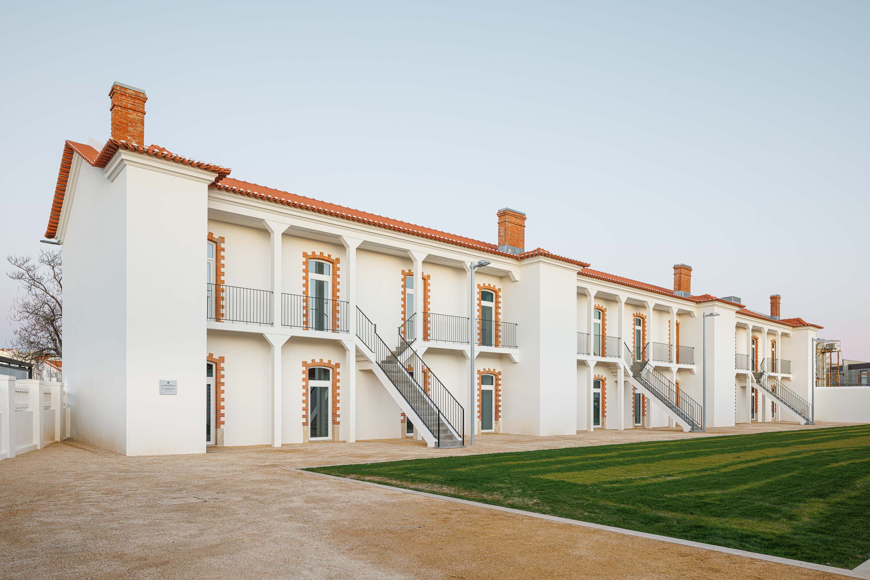 Exterior: Edifício branco com colunas, varandas em ferro e escadas de acesso aos pisos superiores. — Reabilitação Urbana do Bairro do Boneco arquitetura Adarq - André David Arquitecto em Entroncamento