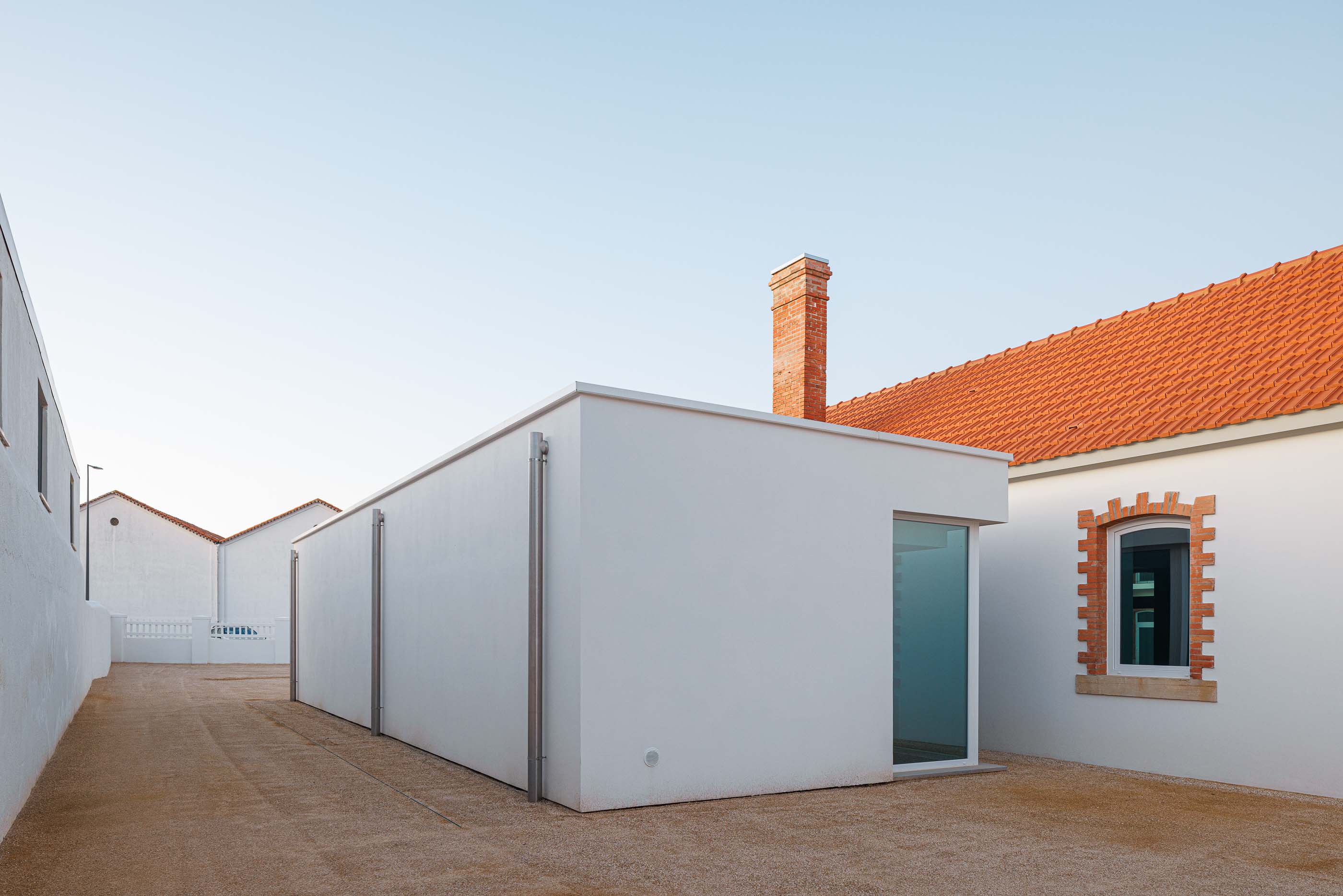 Exterior: Edifício branco com telhado cerâmico e pátio com gravilha. — Reabilitação Urbana do Bairro do Boneco arquitetura Adarq - André David Arquitecto em Entroncamento