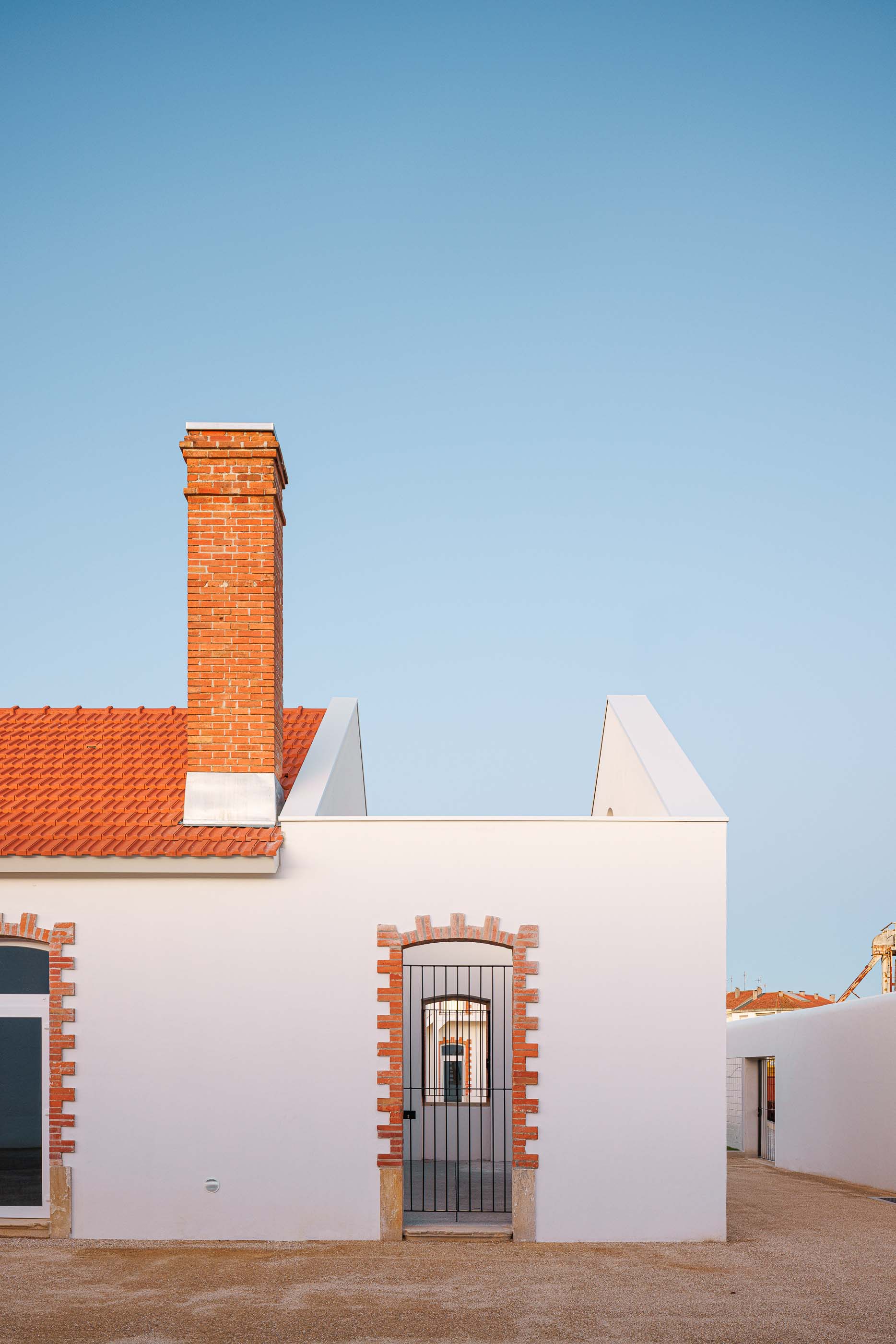 Exterior: Edifício branco com telhado cerâmico e pátio com gravilha. — Reabilitação Urbana do Bairro do Boneco arquitetura Adarq - André David Arquitecto em Entroncamento