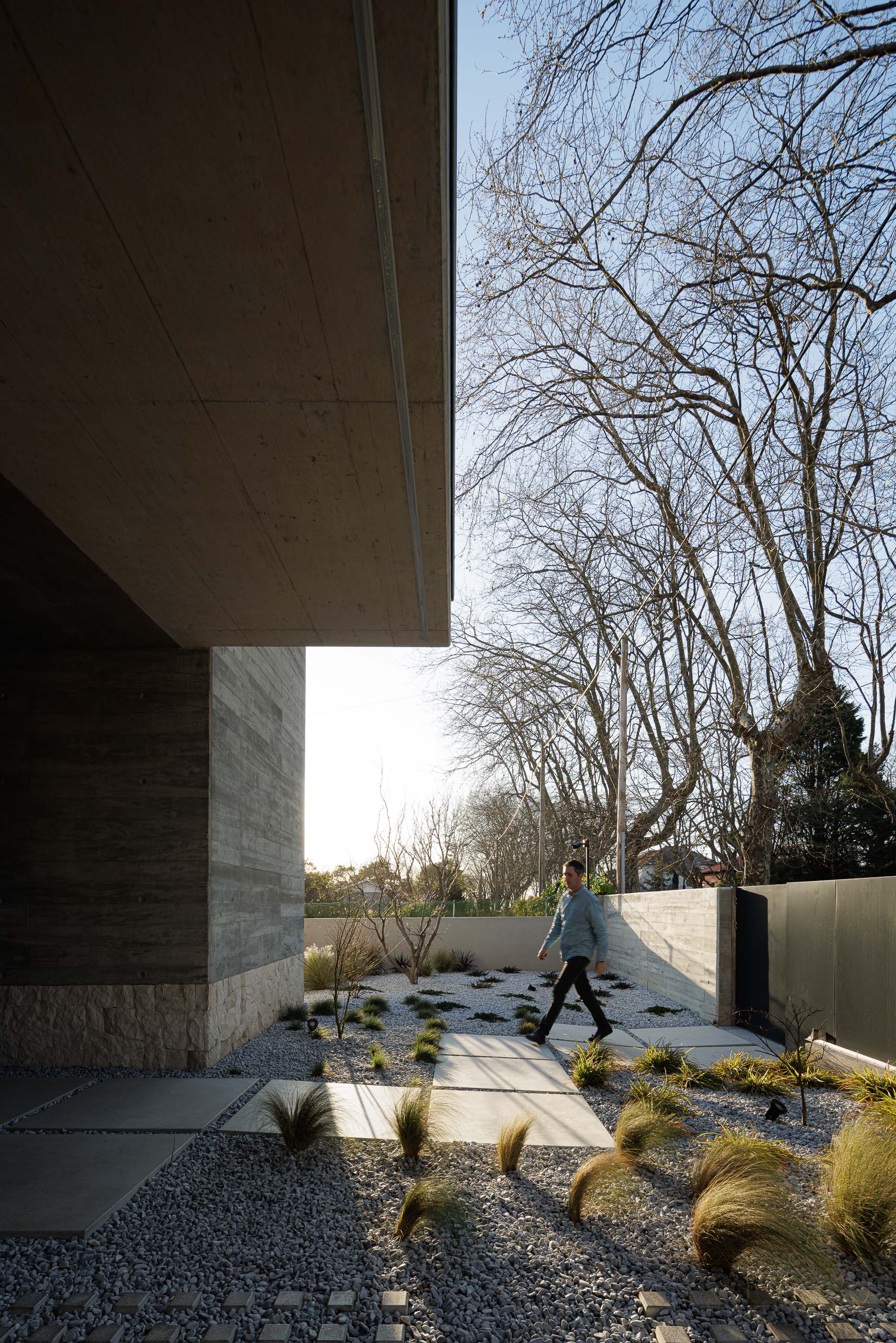 Entrada: Caminho de pedra e gravilha, com estrutura de betão aparente e vegetação rasteira. — Casa M arquitetura silverline em Vila Nova de Gaia