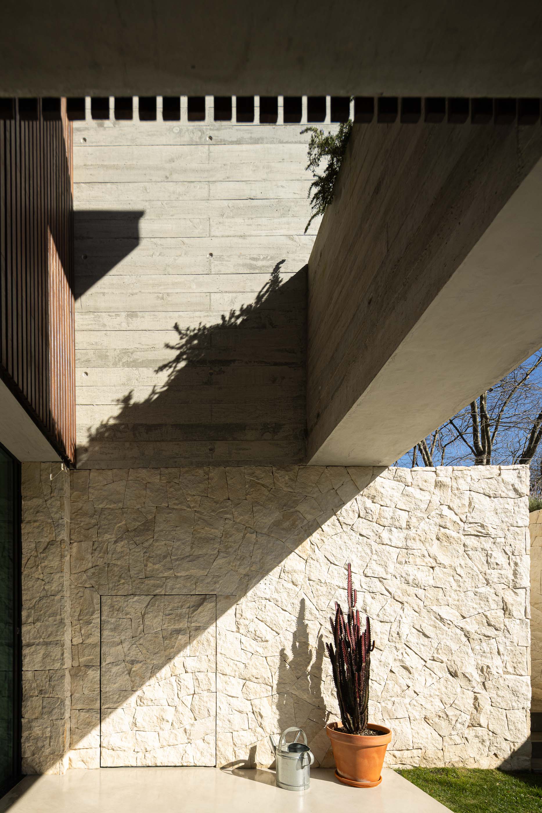 Pátio: Paredes em pedra e betão, com regador e vaso. — Casa M arquitetura silverline em Vila Nova de Gaia