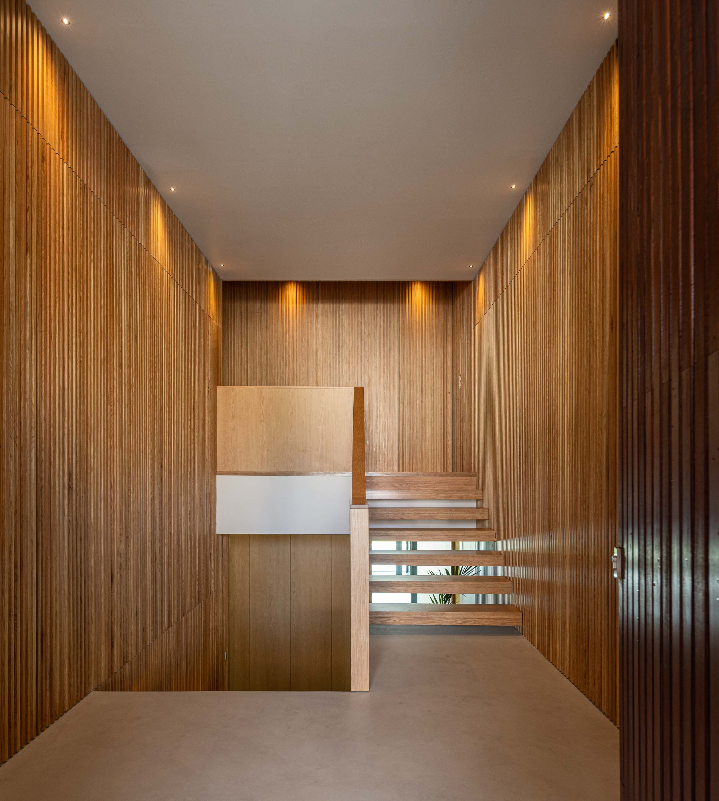 Hall de entrada: Escadas em madeira, paredes revestidas a madeira e iluminação embutida. — Casa M arquitetura silverline em Vila Nova de Gaia