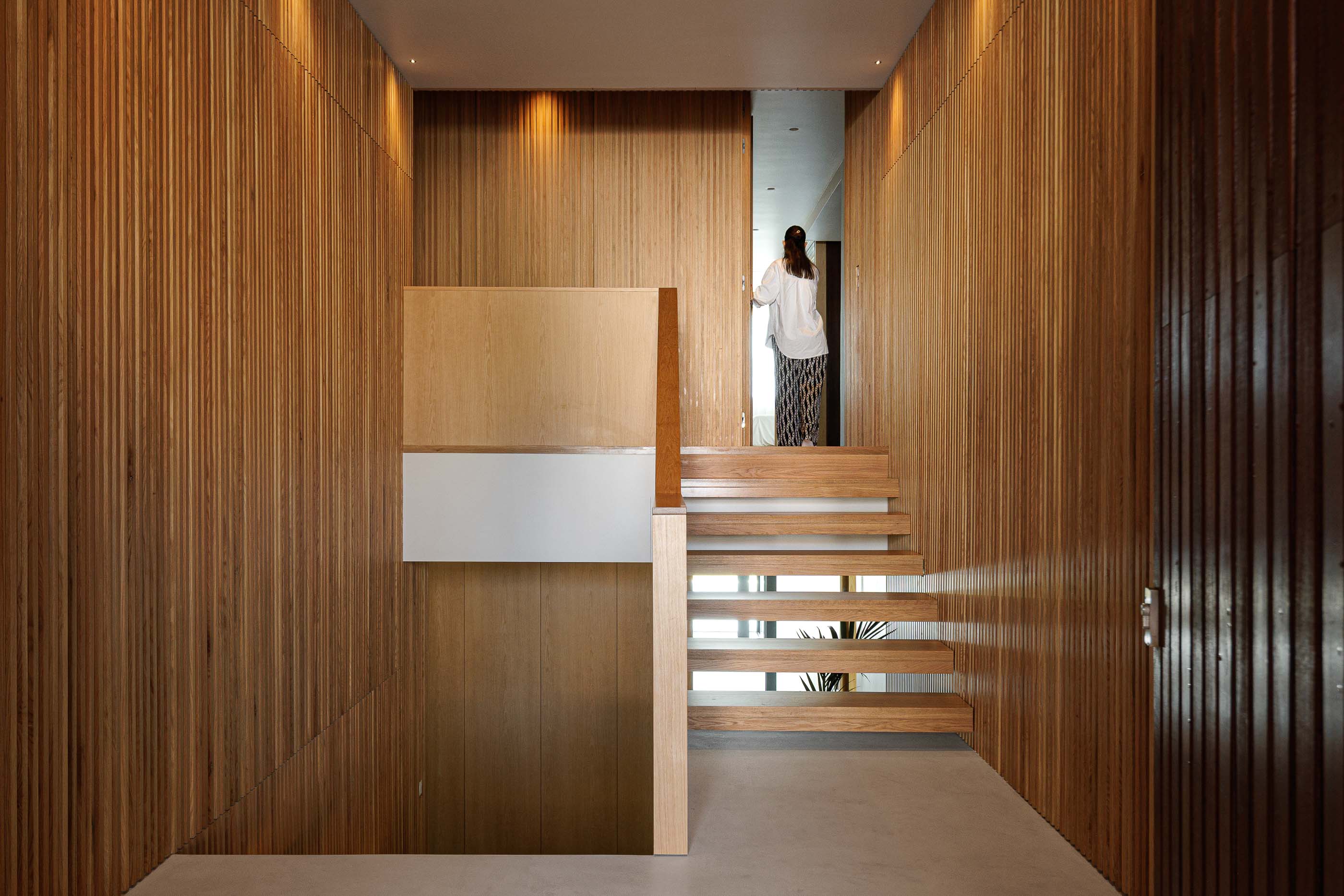 Hall de entrada: Escadas em madeira, paredes revestidas a madeira e porta de correr. — Casa M arquitetura silverline em Vila Nova de Gaia