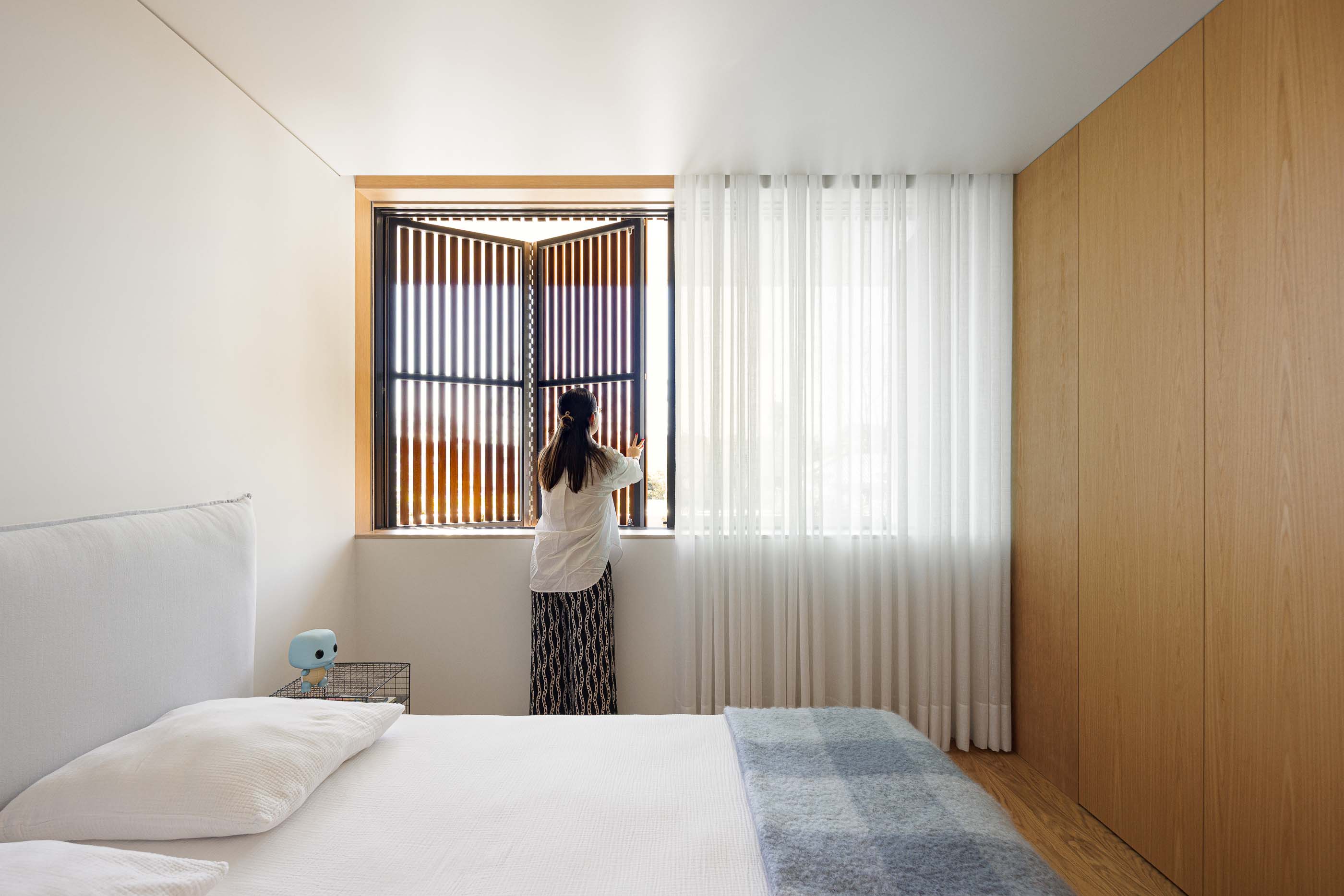 Quarto: Cama com cabeceira branca, cortinas brancas e janela com portadas de madeira. — Casa M arquitetura silverline em Vila Nova de Gaia