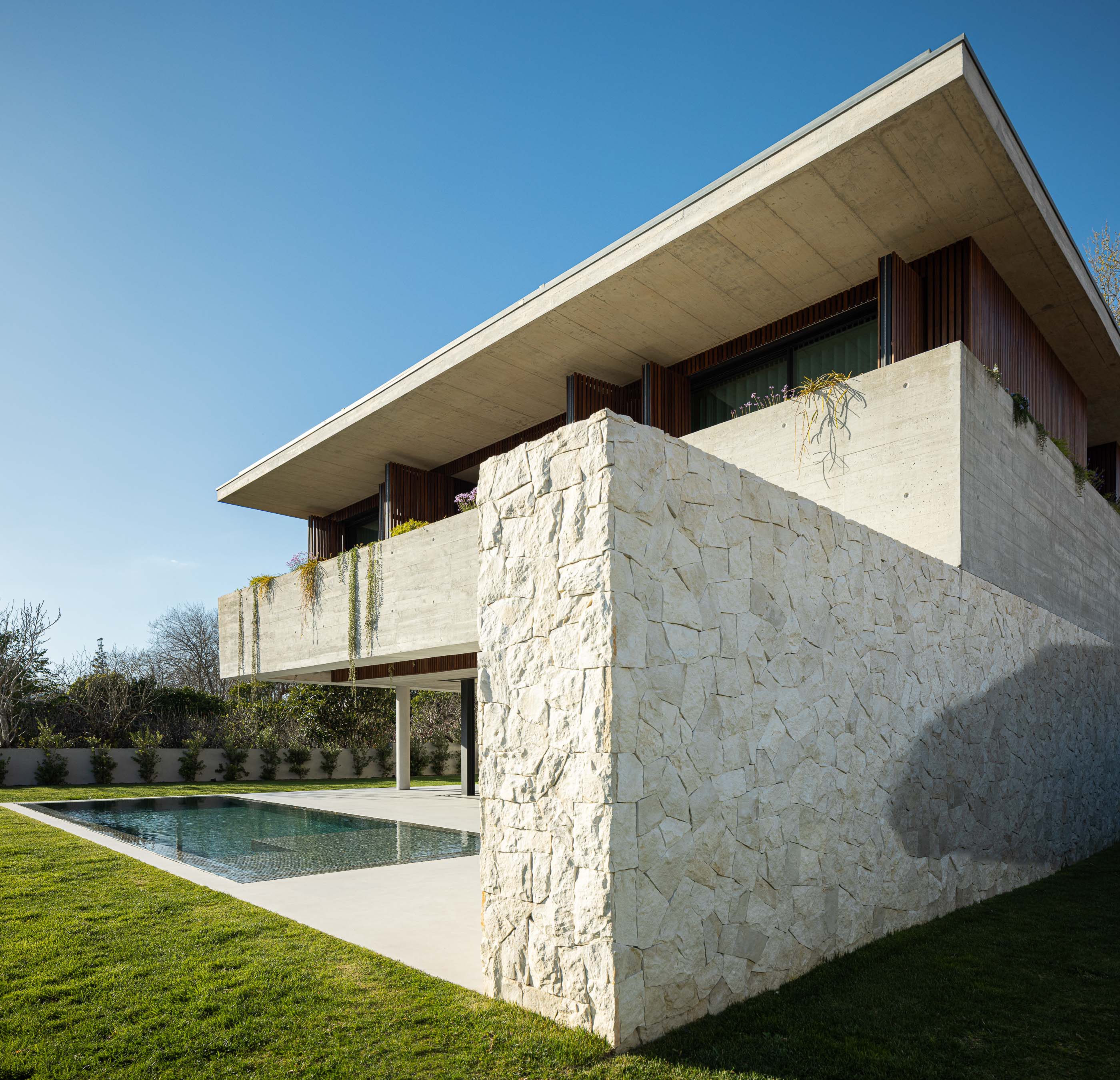 Exterior: Vista lateral da casa com piscina, relvado e muro de pedra. — Casa M arquitetura silverline em Vila Nova de Gaia