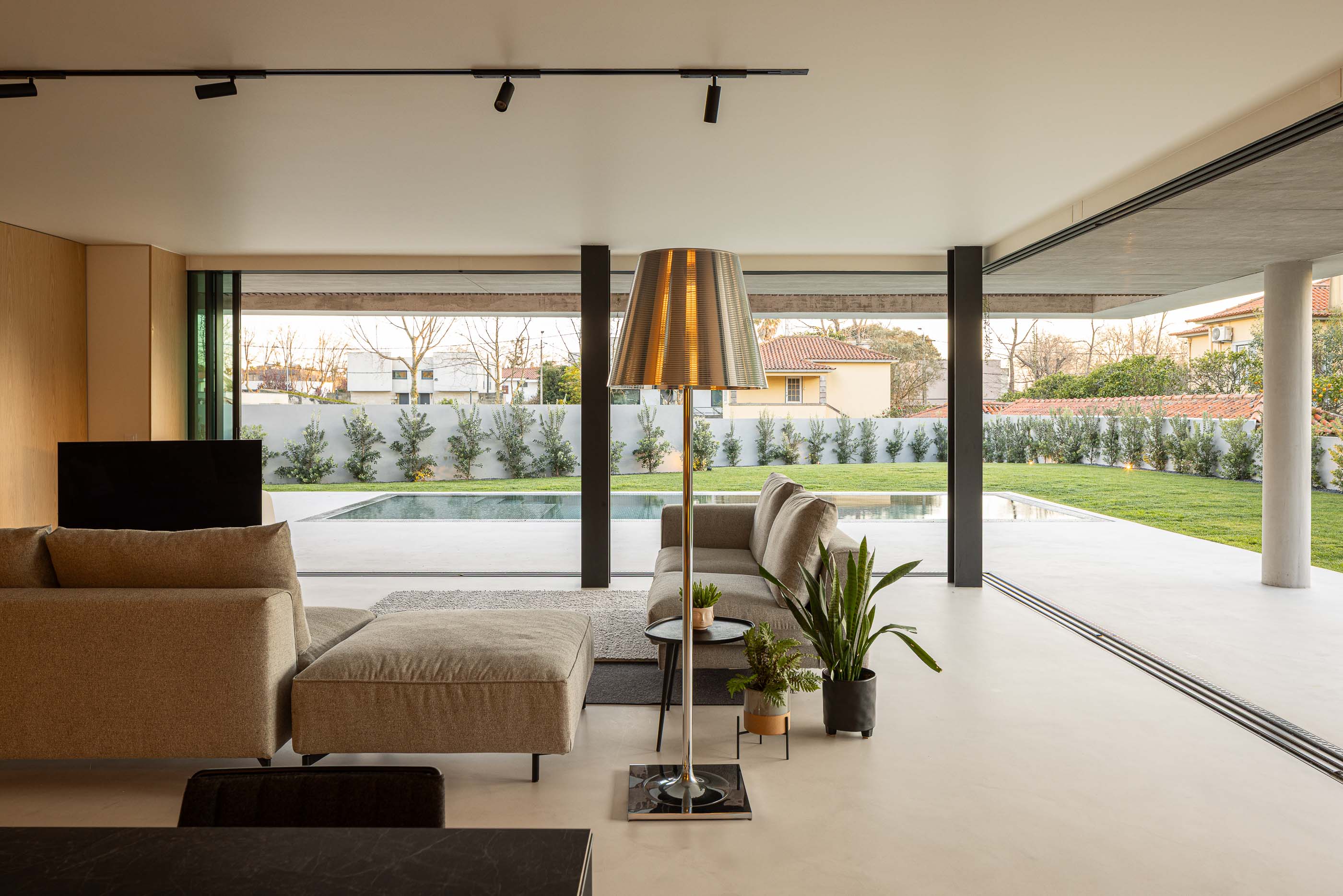 Sala de estar: Sofá cinzento, candeeiro de pé e vista para a piscina. — Casa M arquitetura silverline em Vila Nova de Gaia