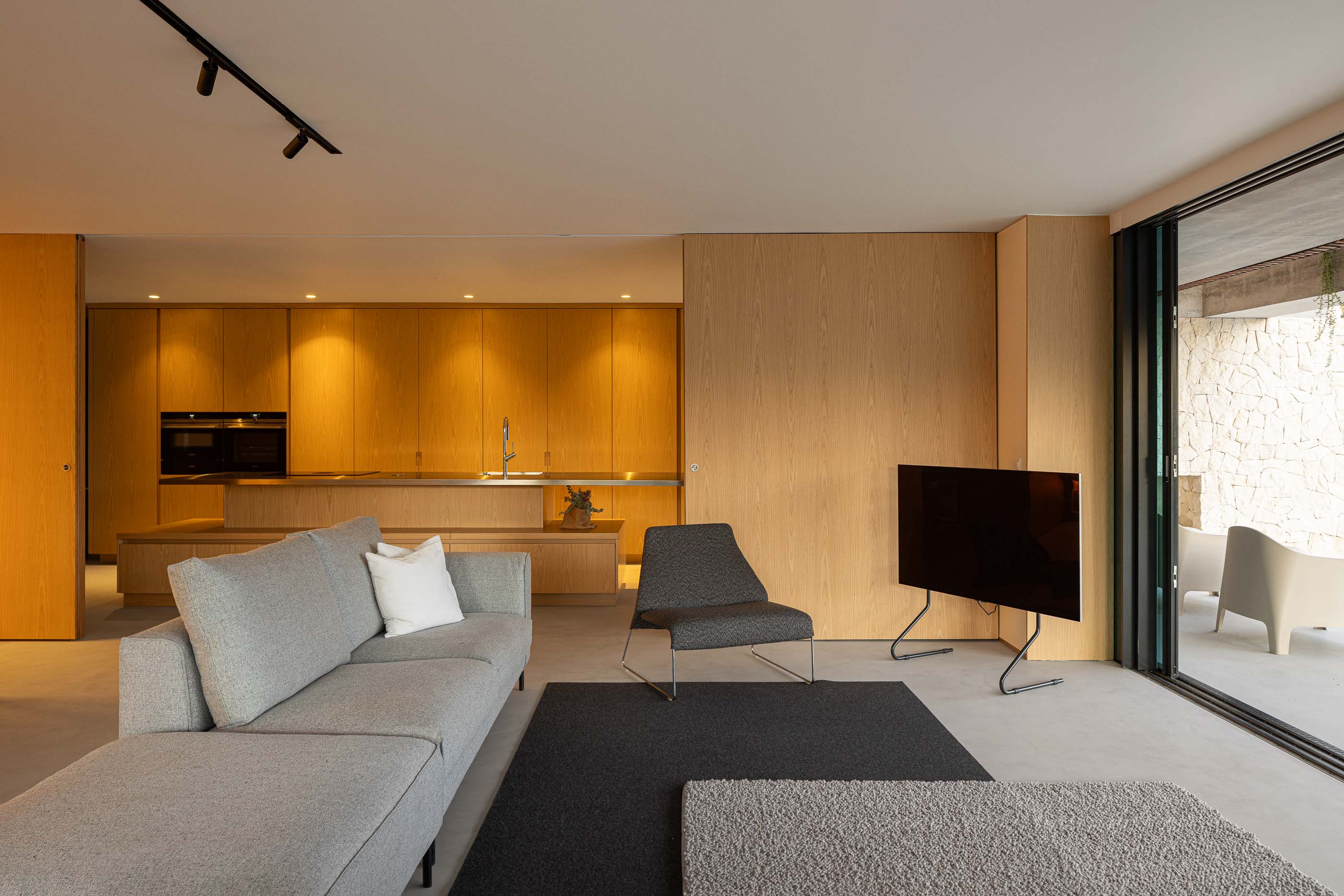 Sala de estar: Sofá cinzento, alcatifa escura e estantes em madeira iluminadas. — Casa M arquitetura silverline em Vila Nova de Gaia