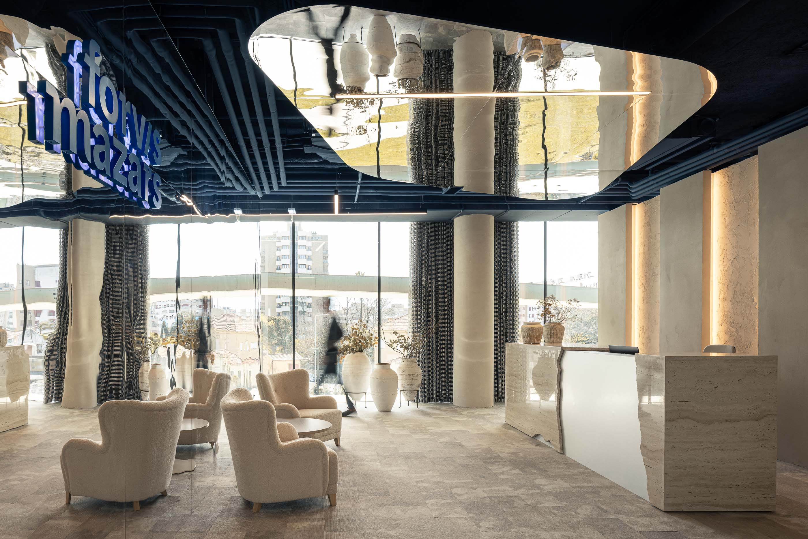 Recepção: Cadeirões em bouclé, candeeiros lineares e balcão em travertino com espelho, sob teto espelhado. — Oporto MAZARS offices arquitetura GRAU.ZERO Arquitectura em Porto
