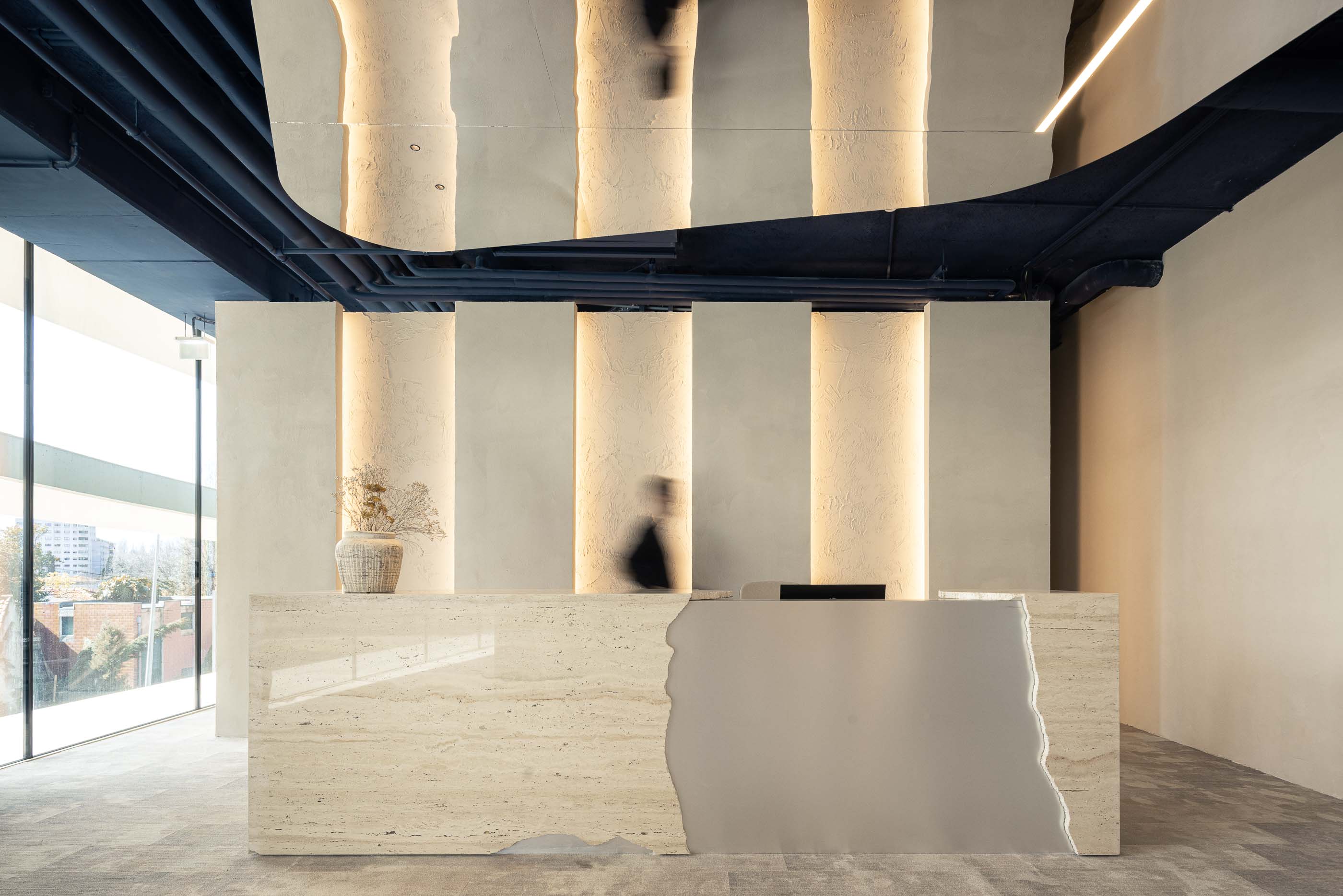 Recepção: Balcão em travertino e espelho, com iluminação vertical nas paredes texturadas. — Oporto MAZARS offices arquitetura GRAU.ZERO Arquitectura em Porto
