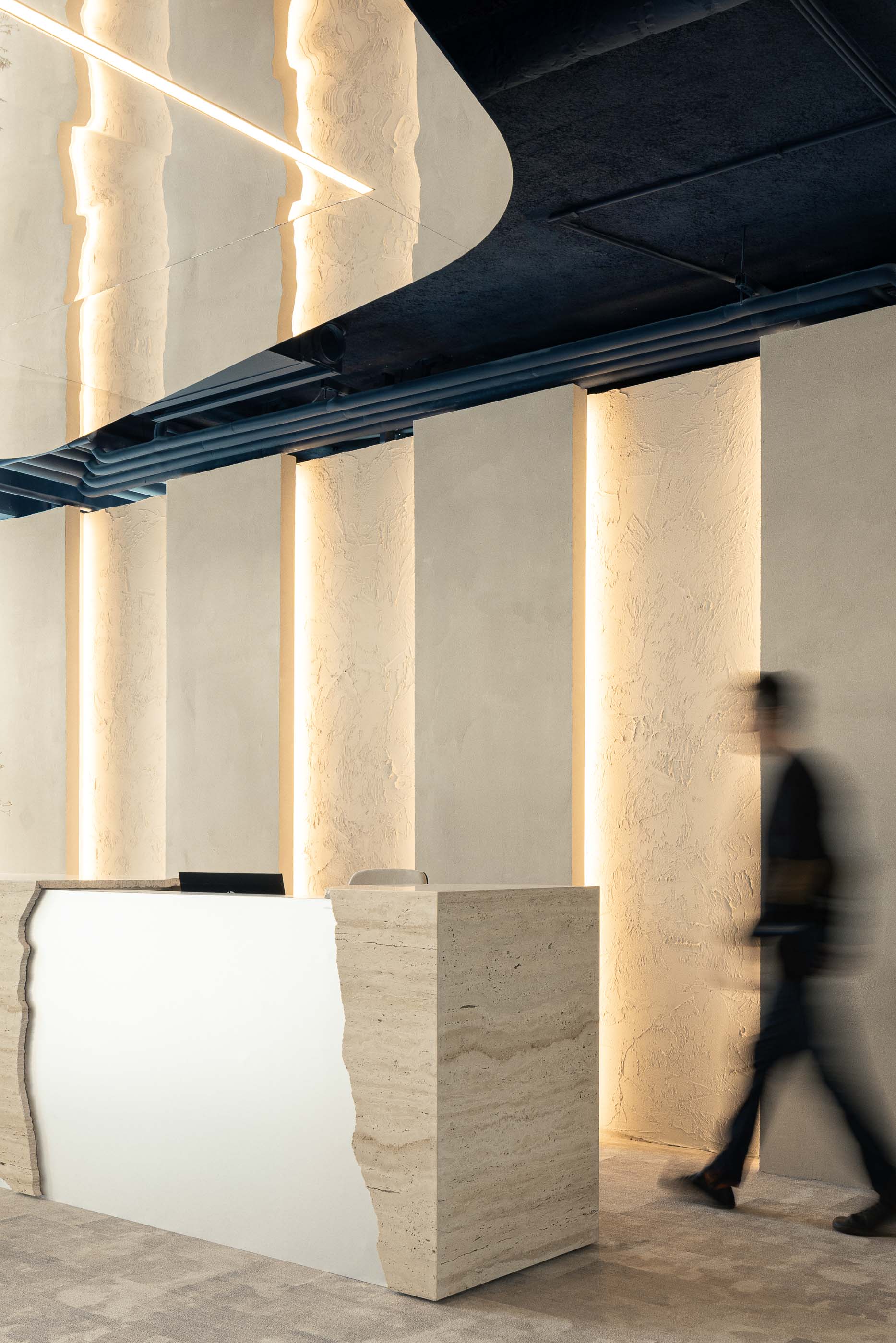 Recepção: Balcão em travertino e espelho, com iluminação vertical e teto azul com tubagens expostas. — Oporto MAZARS offices arquitetura GRAU.ZERO Arquitectura em Porto