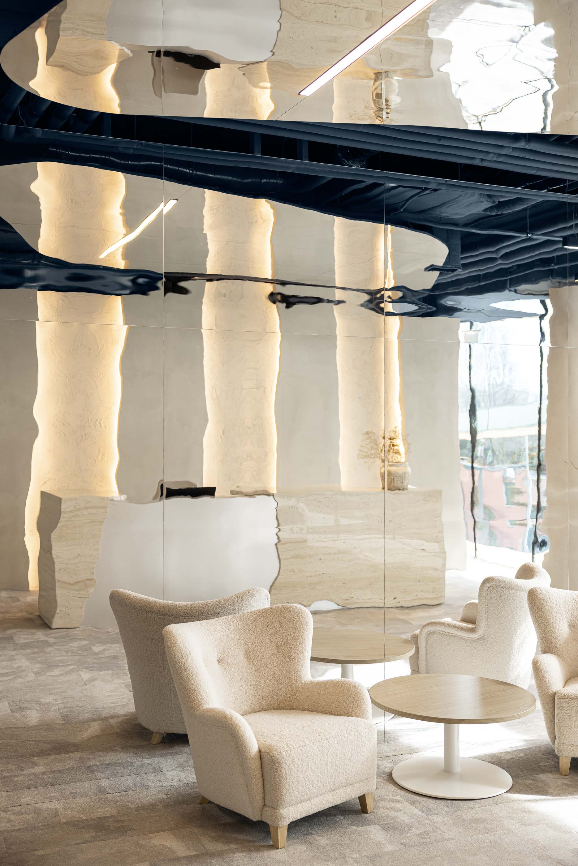 Recepção: Cadeirões em bouclé e balcão em travertino com espelho, sob teto espelhado. — Oporto MAZARS offices arquitetura GRAU.ZERO Arquitectura em Porto