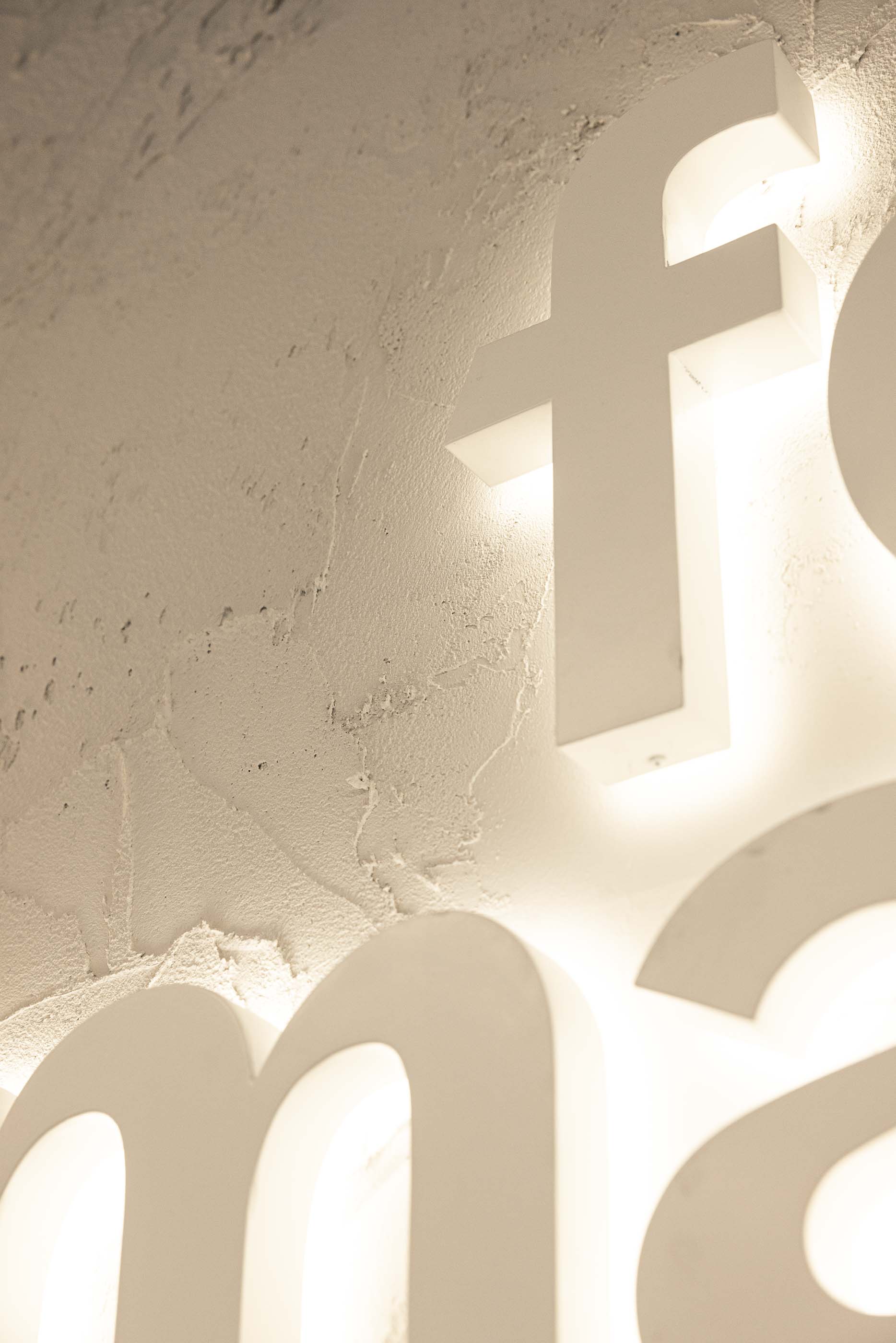 Logótipo: Detalhe do logótipo iluminado na parede texturada branca. — Oporto MAZARS offices arquitetura GRAU.ZERO Arquitectura em Porto