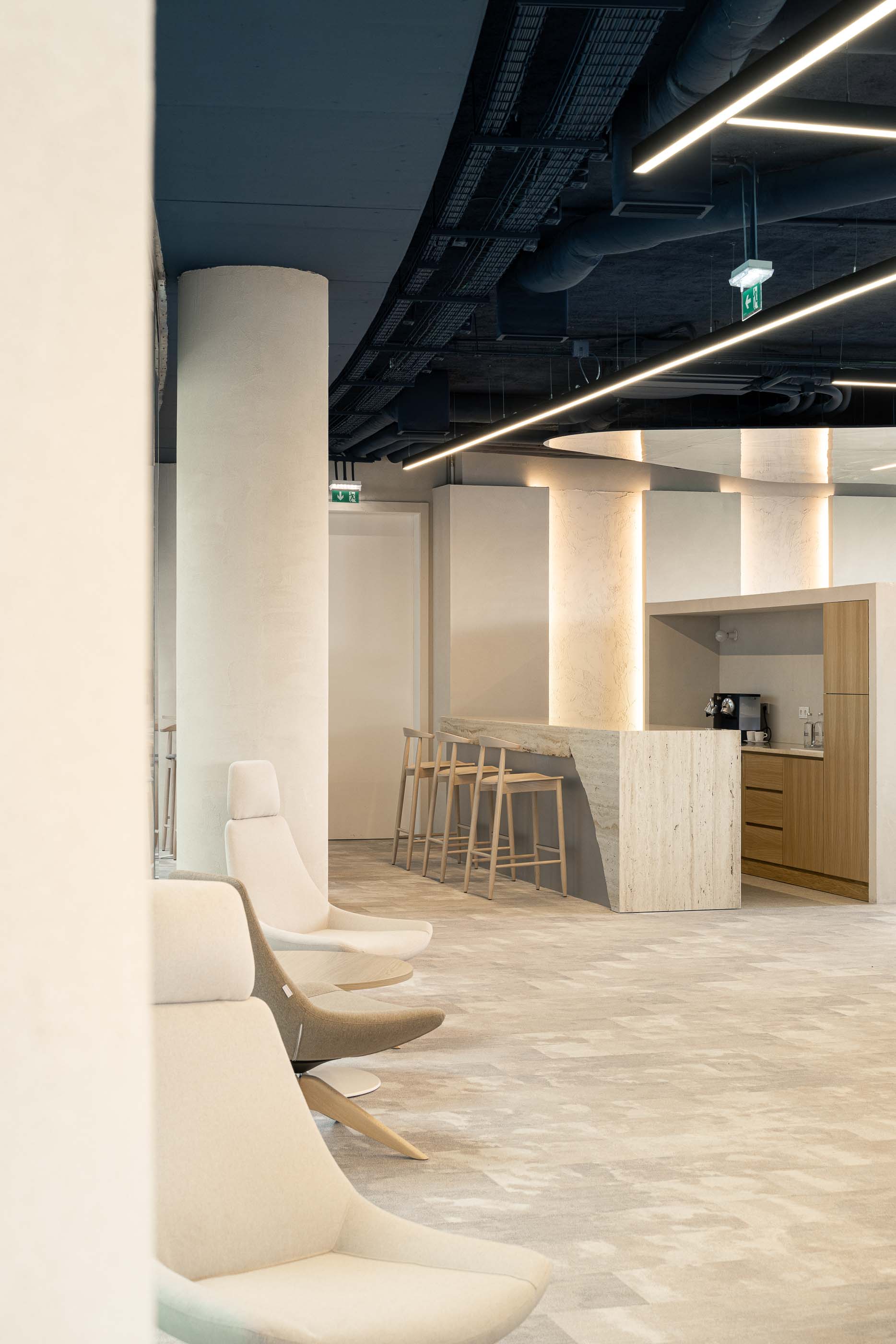 Copa: Balcão alto em travertino, cadeiras de madeira clara e zona de descanso com cadeirões. — Oporto MAZARS offices arquitetura GRAU.ZERO Arquitectura em Porto