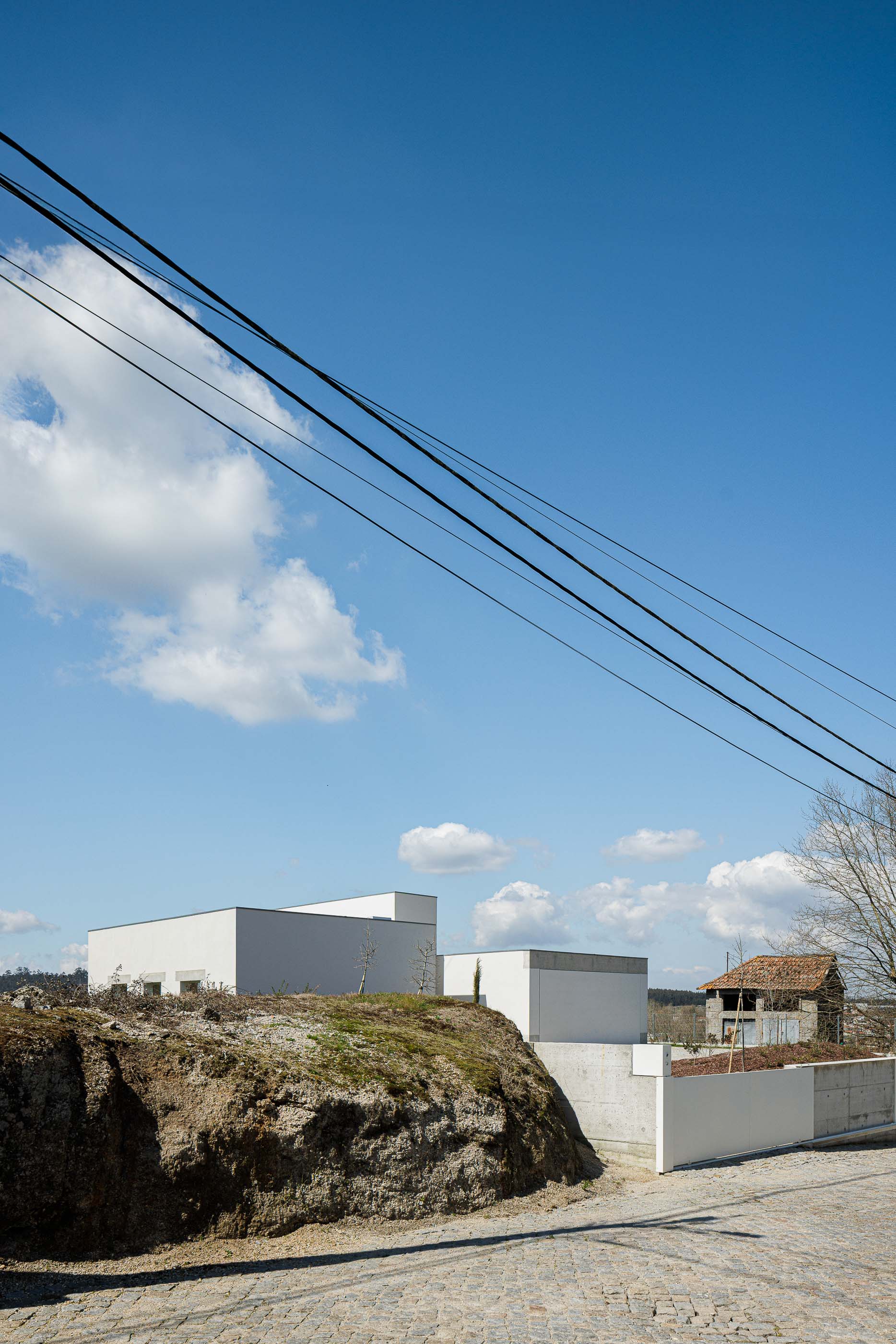 Exterior: Perspectiva da casa branca, com linhas retas e volumes simples, integrada na encosta. — Pedrantil House arquitetura Helder da Rocha Arquitectos em Penafiel
