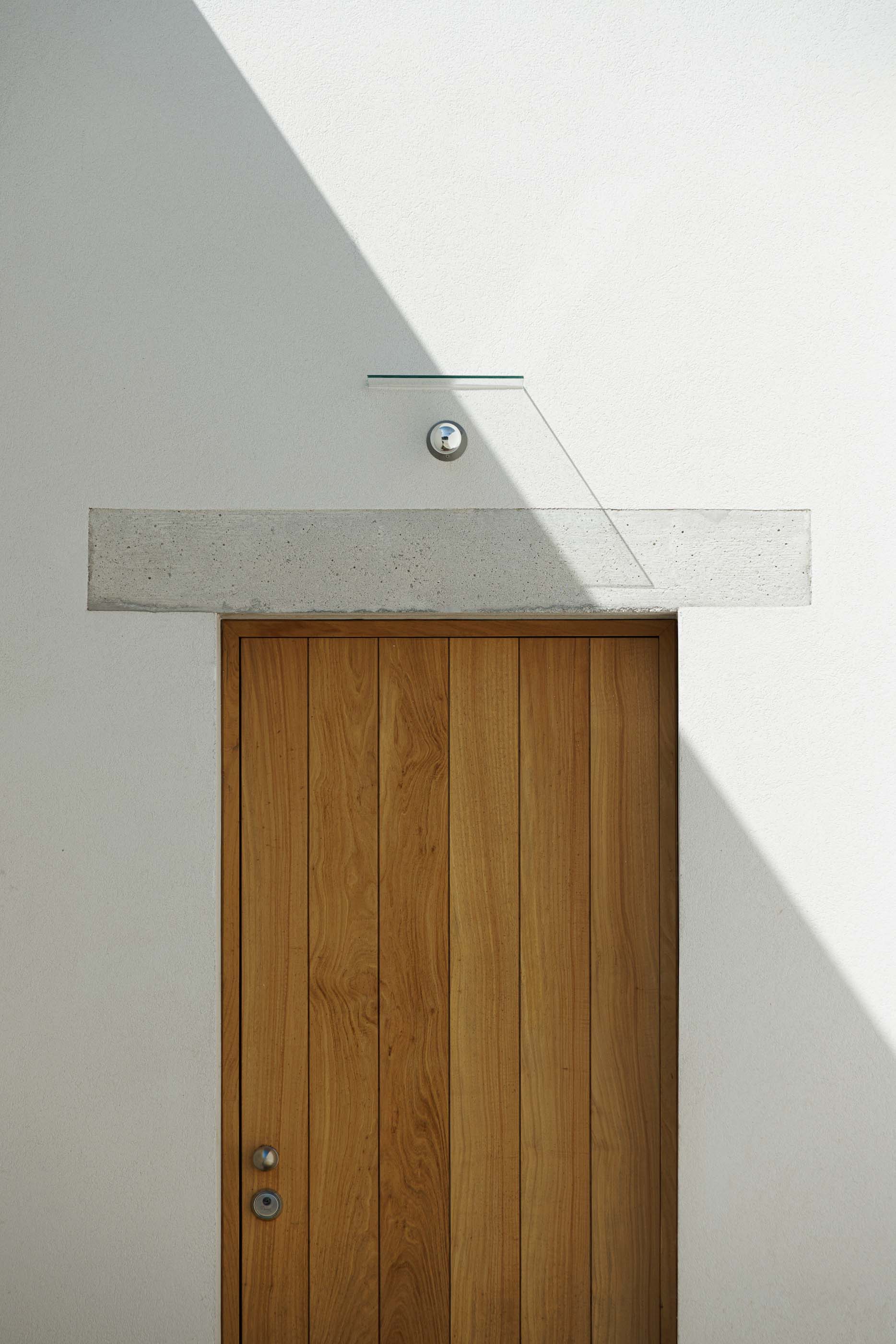 Entrada: Detalhe da porta de madeira, com puxador metálico e iluminação discreta. — Pedrantil House arquitetura Helder da Rocha Arquitectos em Penafiel