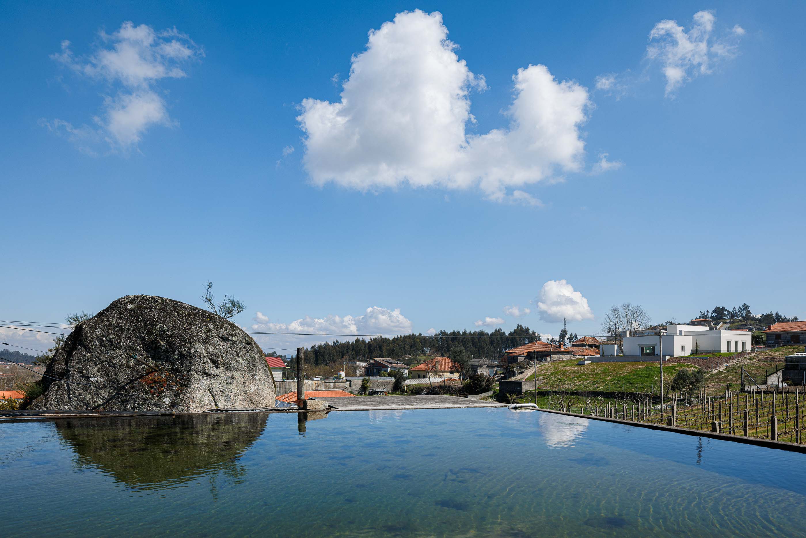 Exterior: Piscina infinita com vista panorâmica sobre a paisagem, refletindo a casa e o céu. — Pedrantil House arquitetura Helder da Rocha Arquitectos em Penafiel