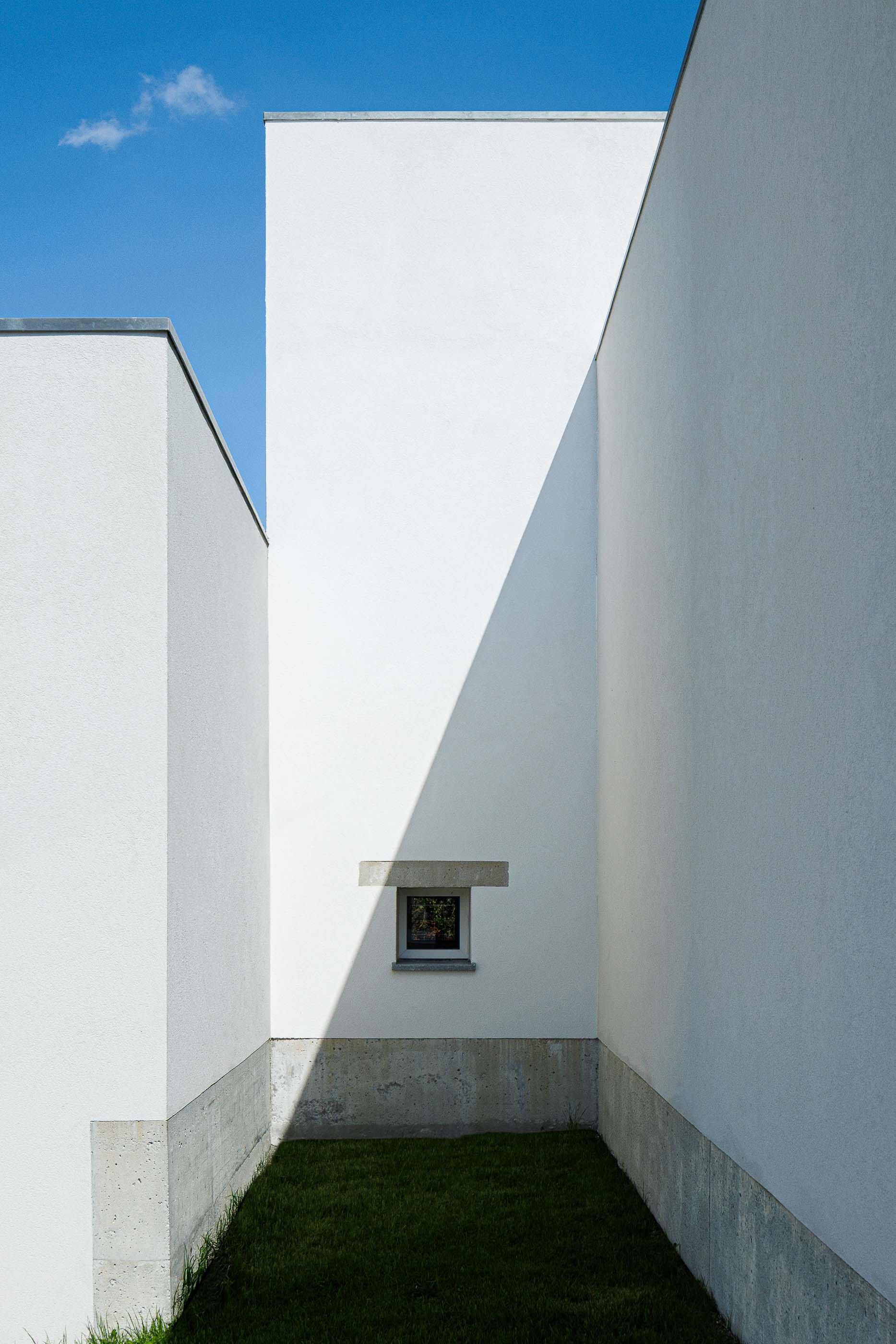 Exterior: Pátio interior com relva, paredes brancas altas e uma pequena janela emoldurada em betão. — Pedrantil House arquitetura Helder da Rocha Arquitectos em Penafiel