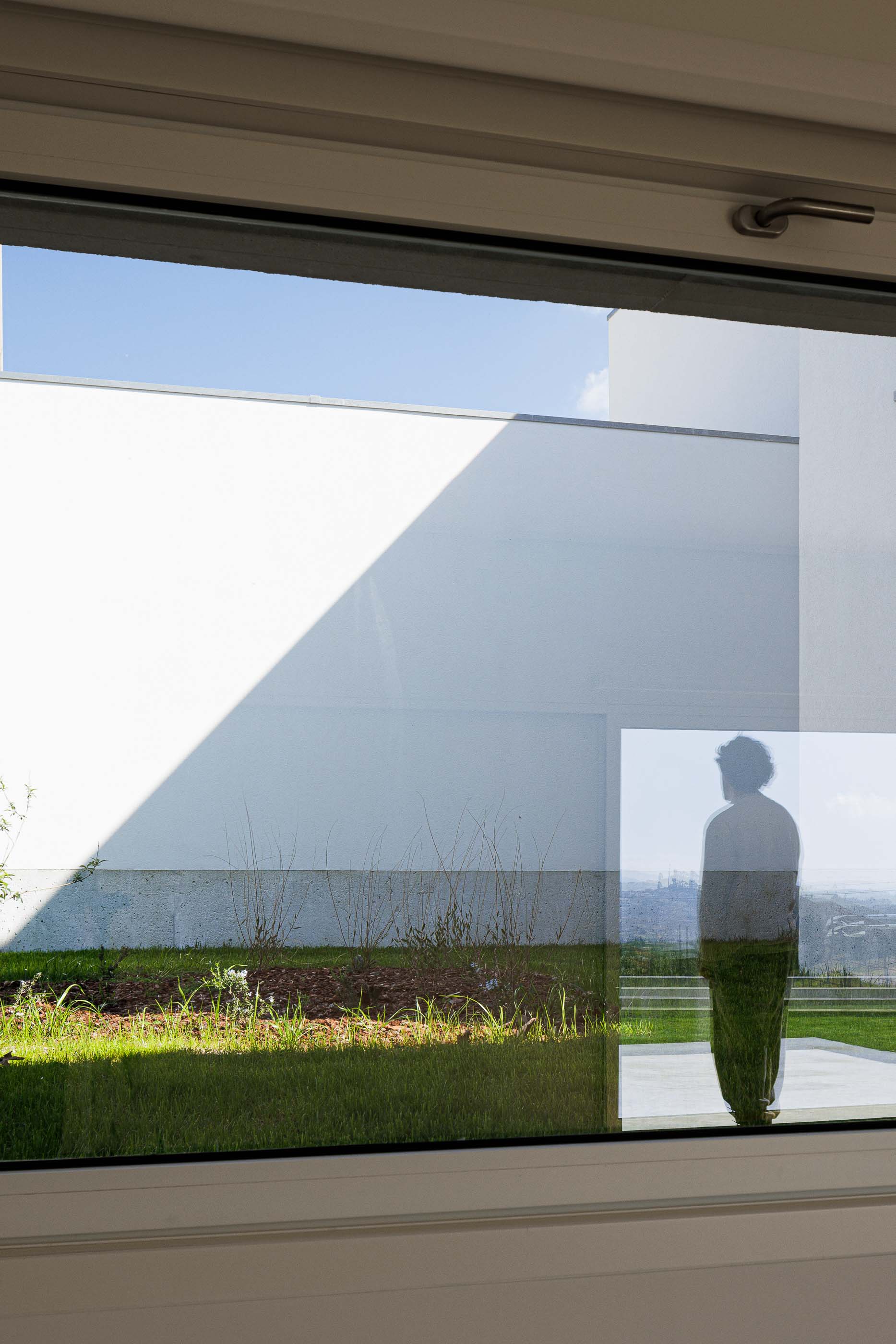 Exterior: Reflexo da casa no vidro da janela, mostrando o jardim e a silhueta de uma pessoa. — Pedrantil House arquitetura Helder da Rocha Arquitectos em Penafiel