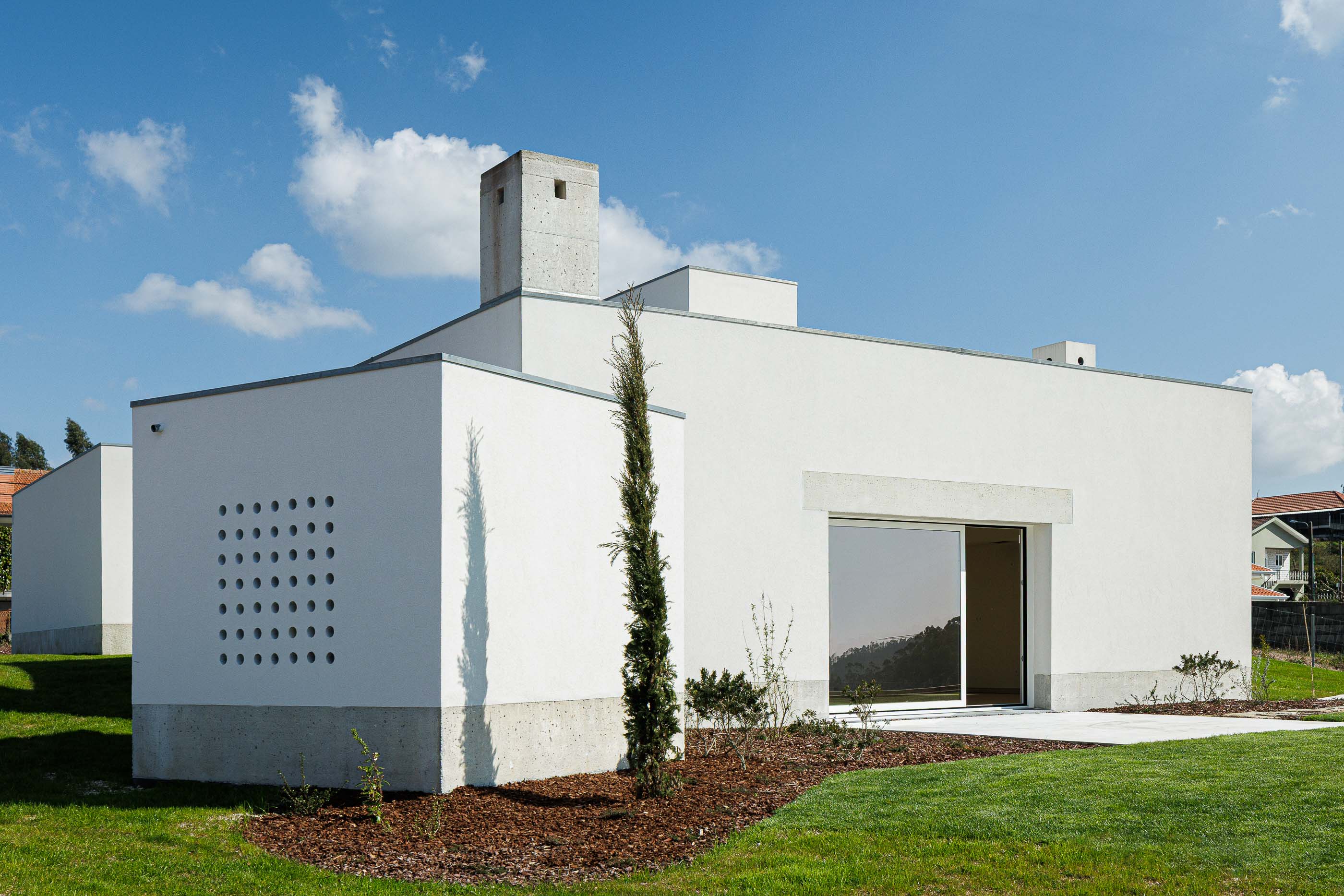 Exterior: Fachada da casa com detalhes em betão, janelas amplas e um padrão de orifícios quadrados. — Pedrantil House arquitetura Helder da Rocha Arquitectos em Penafiel