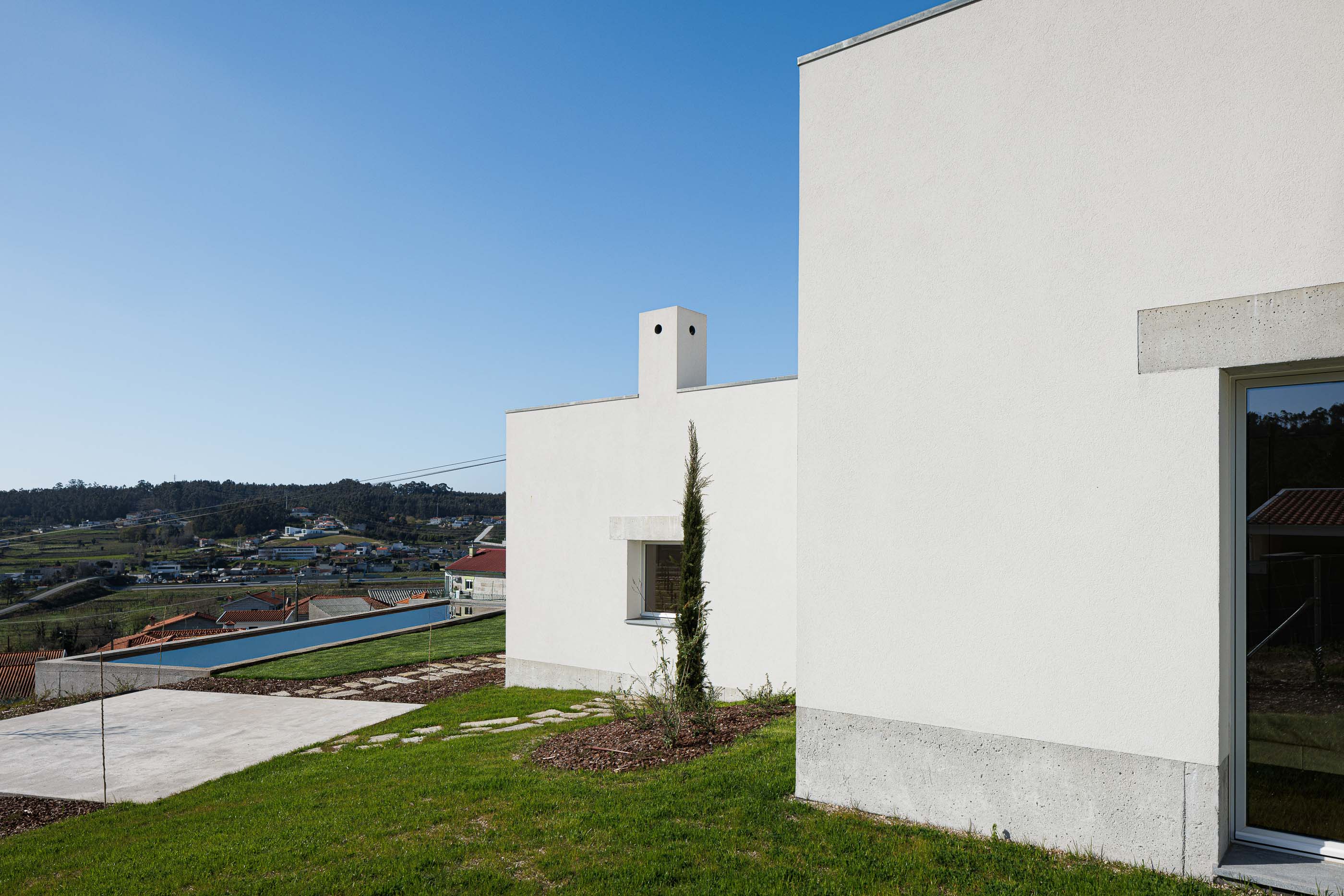 Exterior: Vista lateral da casa, com piscina ao fundo e paisagem rural, num dia soalheiro. — Pedrantil House arquitetura Helder da Rocha Arquitectos em Penafiel