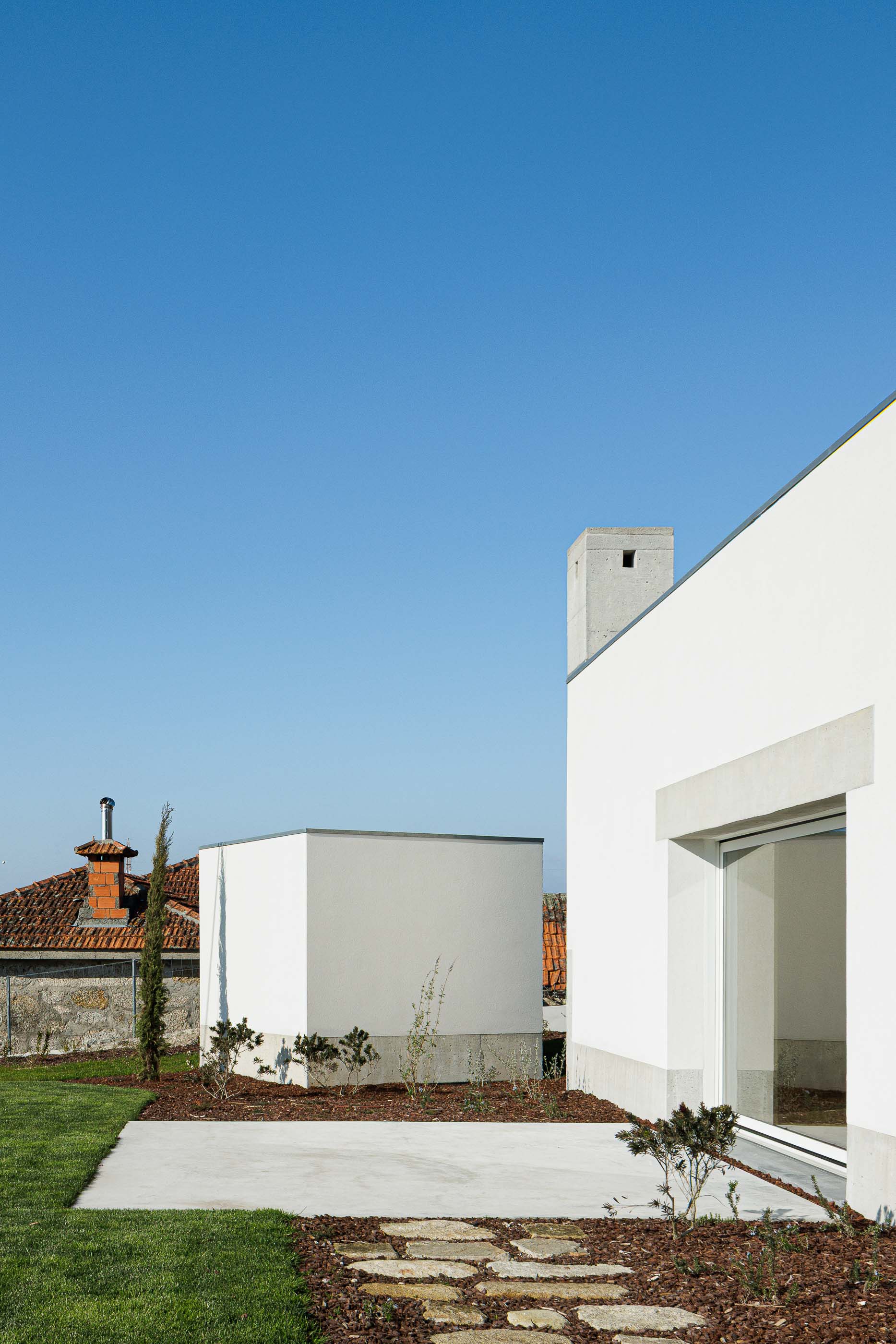 Exterior: Pátio com pavimento em betão, relvado e vegetação, com a casa ao fundo. — Pedrantil House arquitetura Helder da Rocha Arquitectos em Penafiel