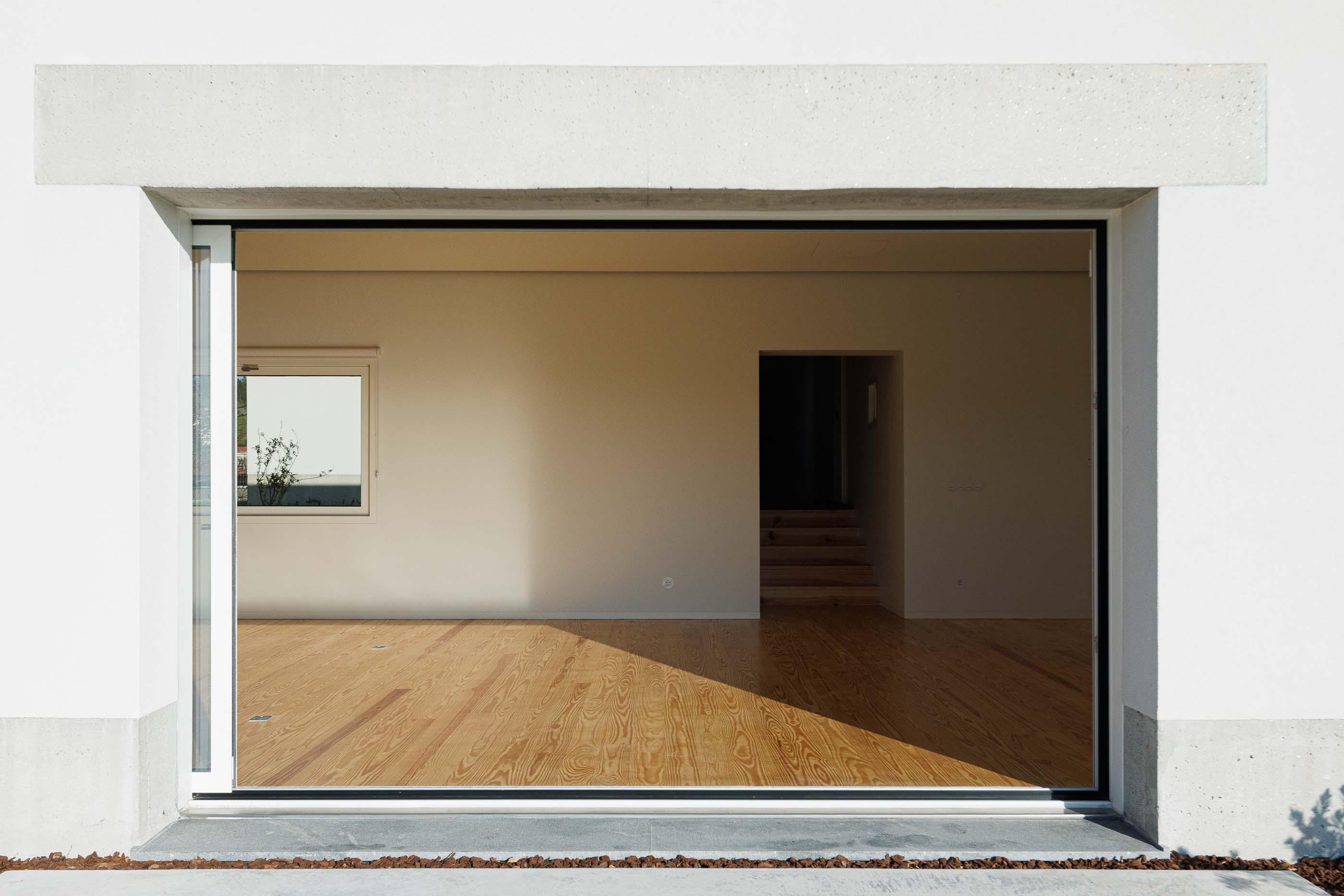 Sala: Ampla janela com vista para o exterior, pavimento em madeira e escadas de acesso. — Pedrantil House arquitetura Helder da Rocha Arquitectos em Penafiel