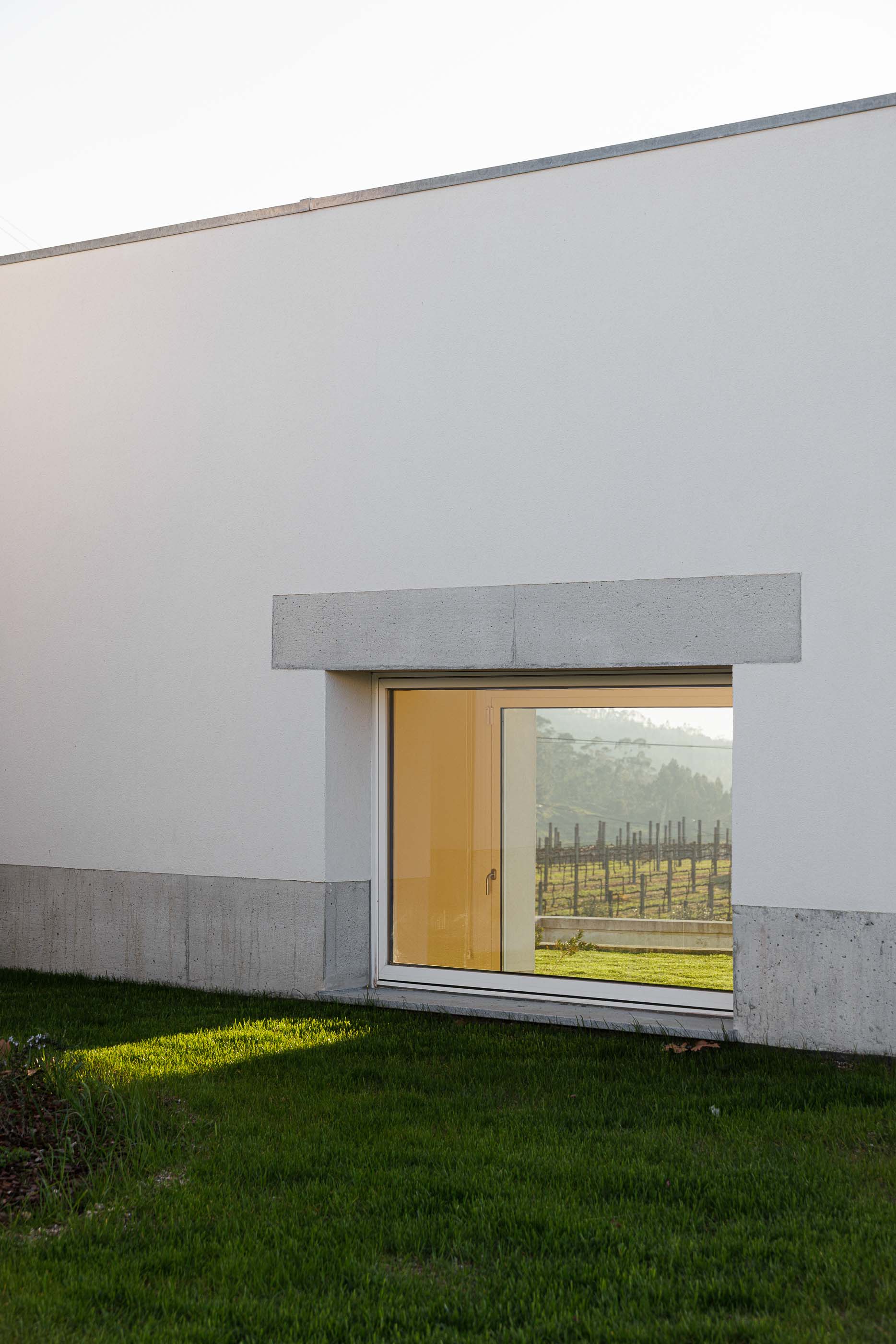 Exterior: Janela com moldura em betão, vista para a paisagem e relvado em primeiro plano. — Pedrantil House arquitetura Helder da Rocha Arquitectos em Penafiel