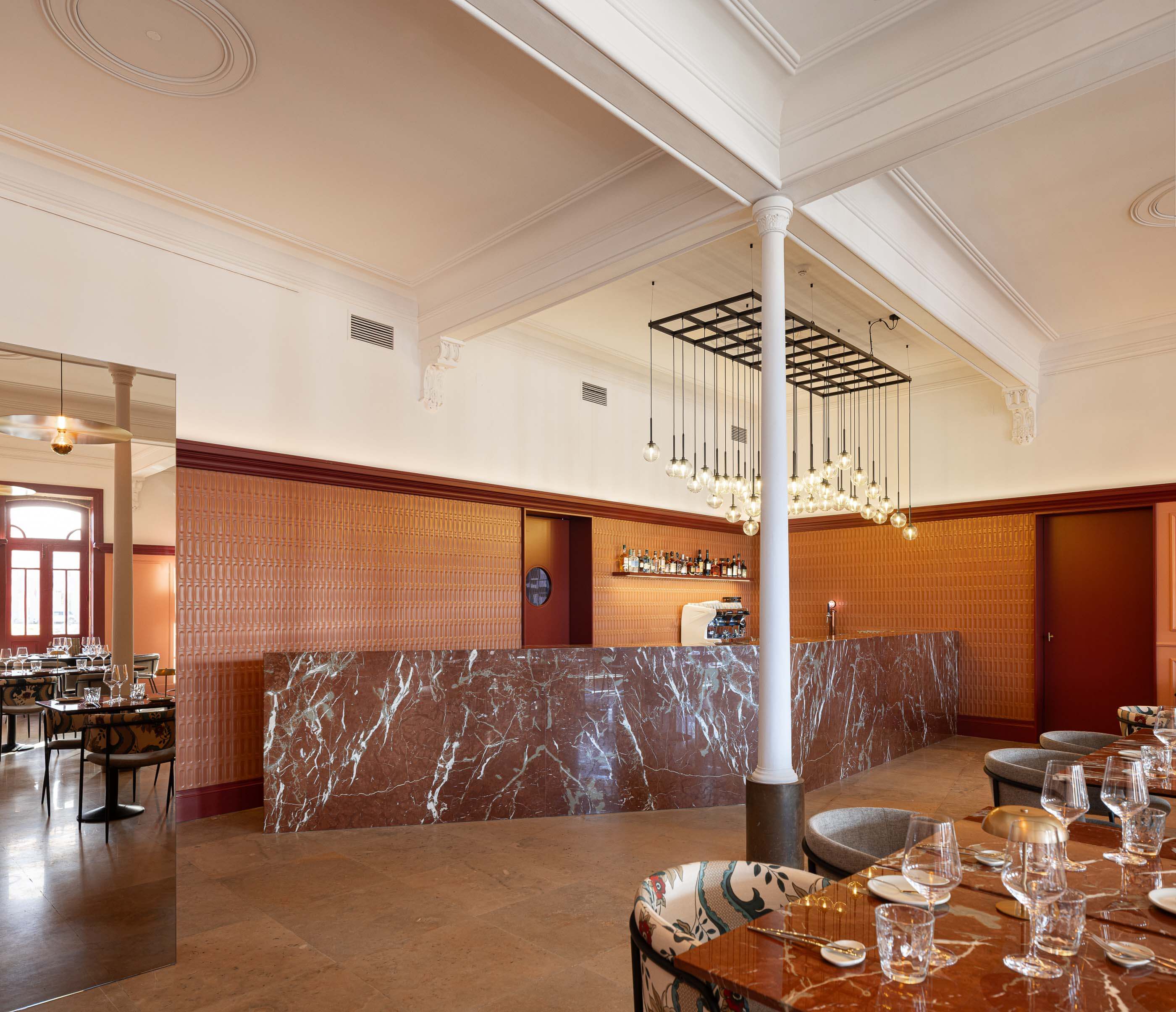 Restaurante: Vista do bar com balcão de mármore, parede texturada, porta com óculo e iluminação suspensa. — Restaurante Concerto arquitetura MiMool Arquitectura & Interiores em vila do conde