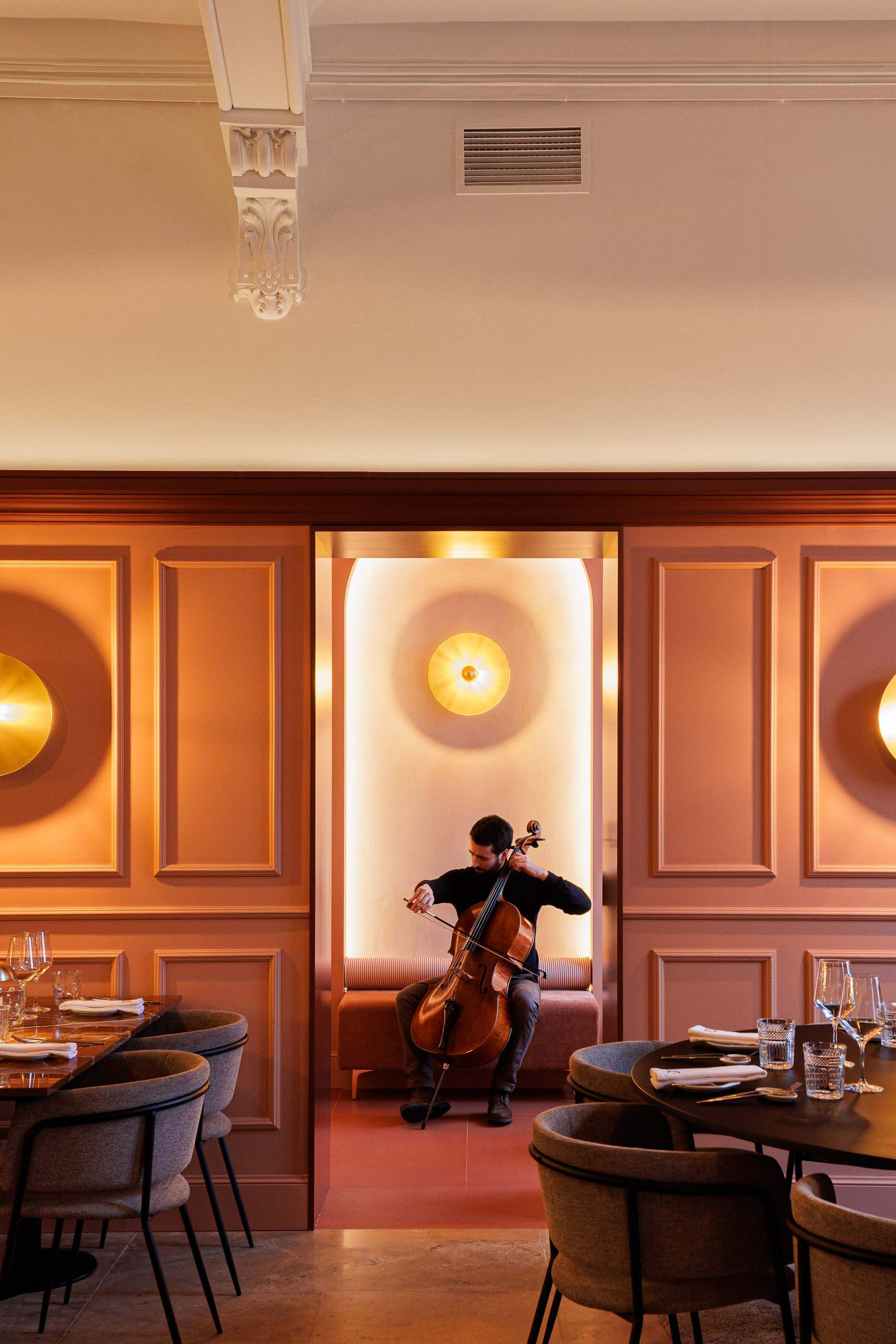 Restaurante: Músico a tocar violoncelo num nicho com banco almofadado e candeeiro dourado. — Restaurante Concerto arquitetura MiMool Arquitectura & Interiores em vila do conde