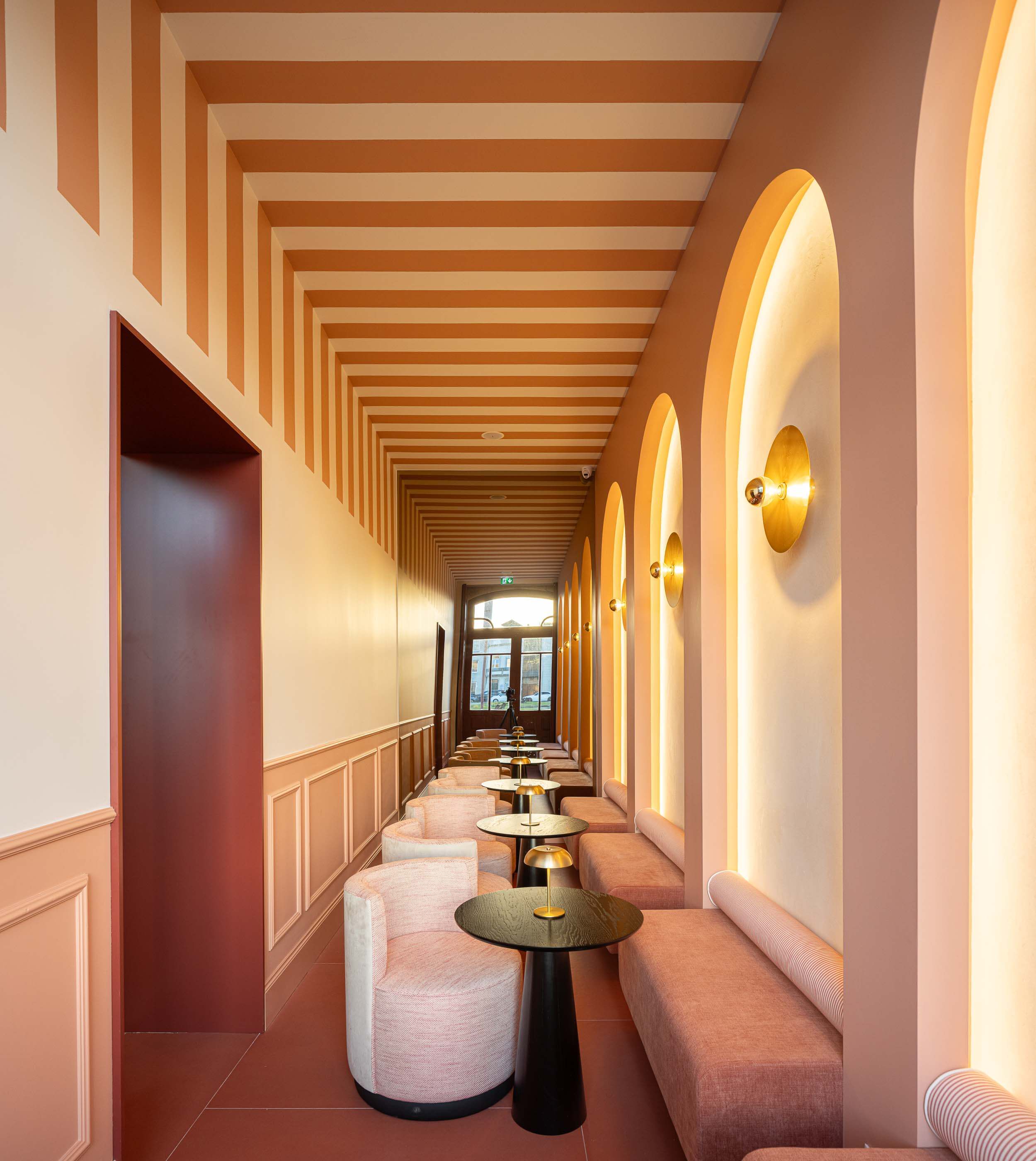 Corredor: Corredor com sofás, mesas de apoio, iluminação dourada e pavimento em tons de terracota. — Restaurante Concerto arquitetura MiMool Arquitectura & Interiores em vila do conde
