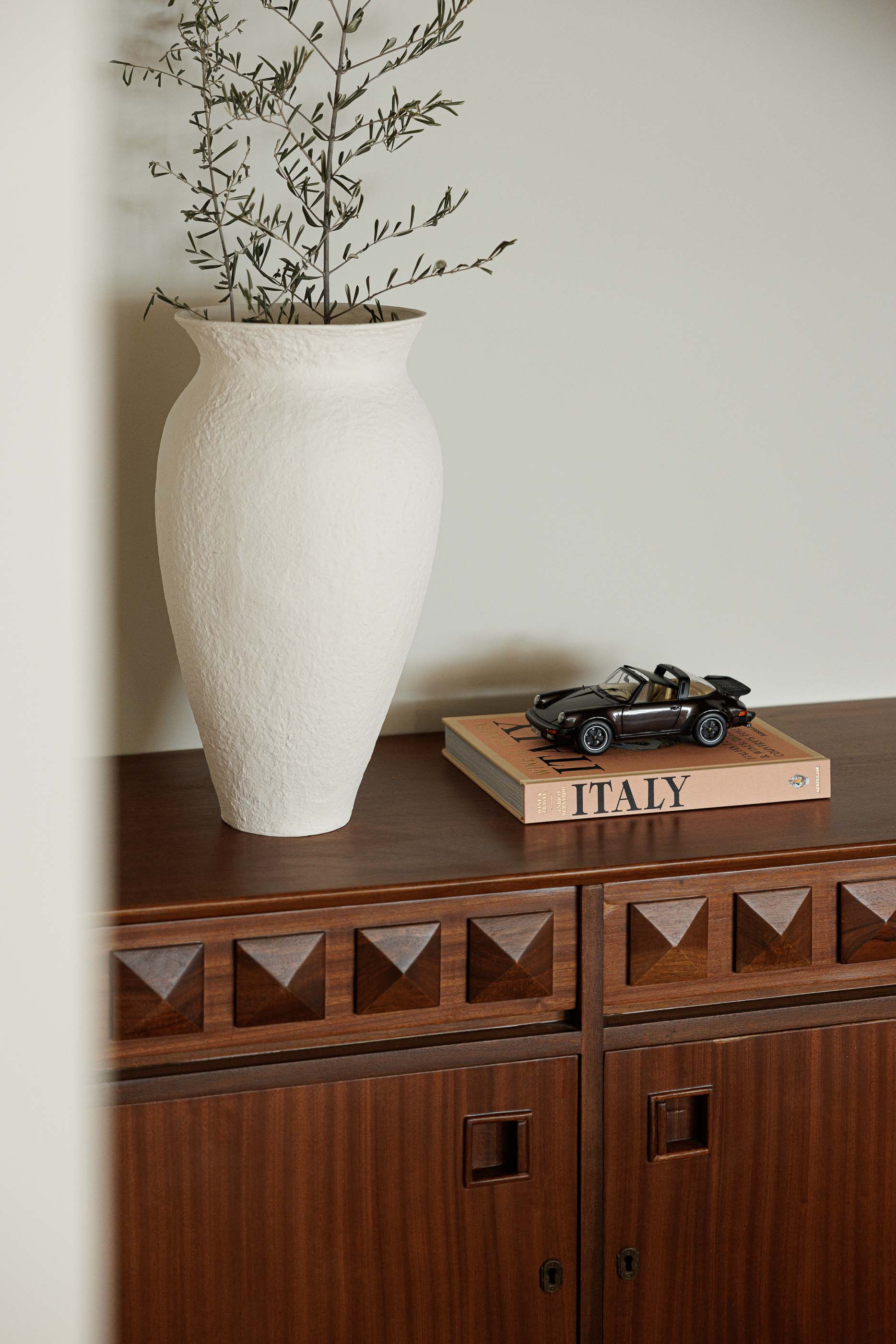Sala de jantar: Detalhe de vaso e livro sobre credenza de madeira escura, com escadas ao fundo. — Casa no Gerês arquitetura MAT Arquitetura e Interiores em Gerês
