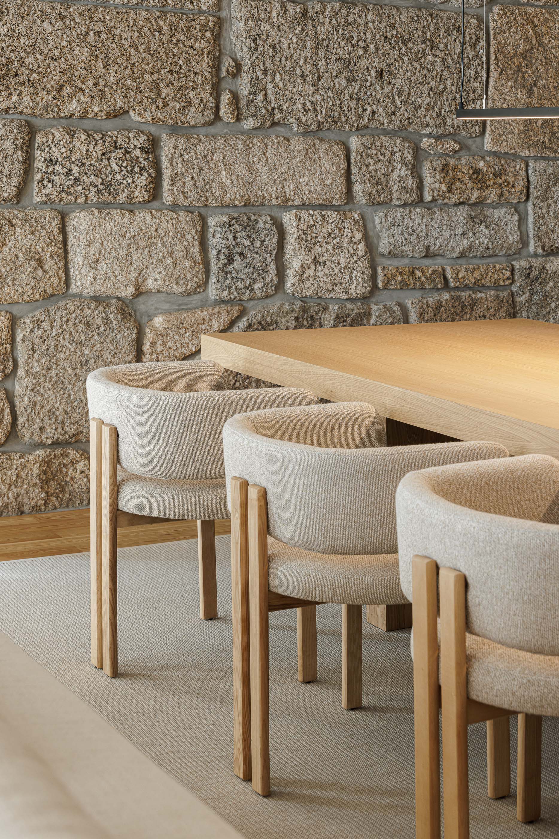 Sala de jantar: Detalhe da parede de pedra rústica e cadeiras estofadas com estrutura em madeira. — Casa no Gerês arquitetura MAT Arquitetura e Interiores em Gerês