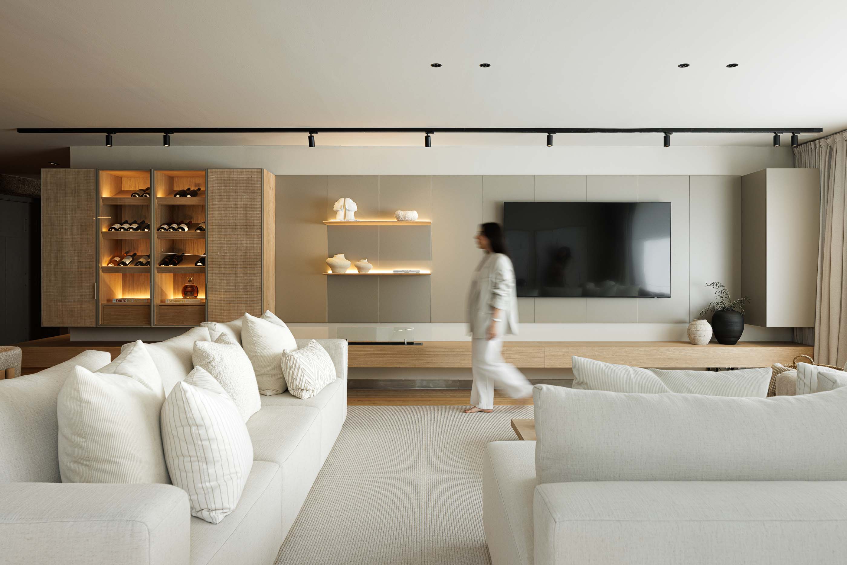 Sala de estar: Sofá branco com almofadas, móvel de madeira com garrafeira e televisão. — Casa no Gerês arquitetura MAT Arquitetura e Interiores em Gerês