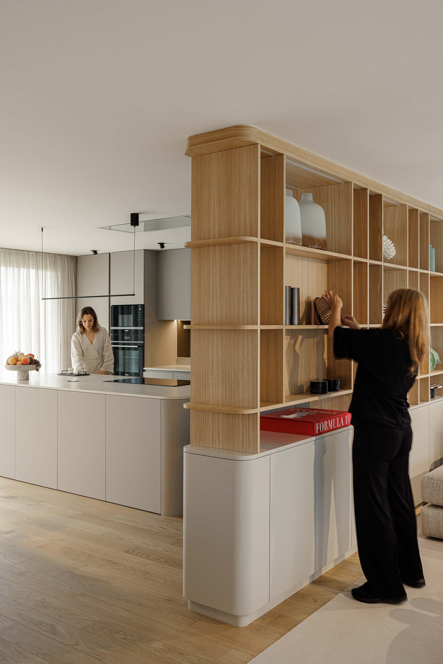 Cozinha e sala de estar em open space. Estante em madeira separa os espaços. Ilha central na cozinha. — Casa Linho arquitetura Paula Novais Arquitectos em Fafe