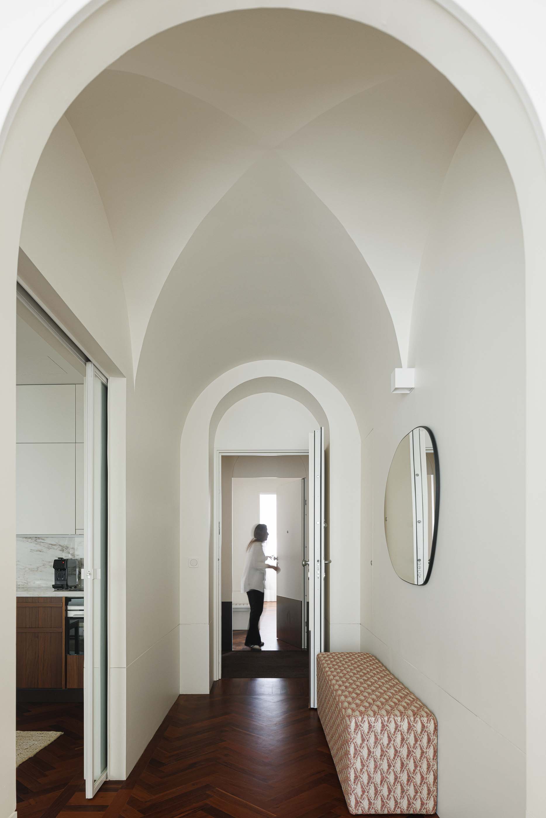 Corredor: Corredor com teto abobadado, pavimento em madeira, espelho redondo e banco estofado. — Vila Catarina Apartments arquitetura Masslab em Porto