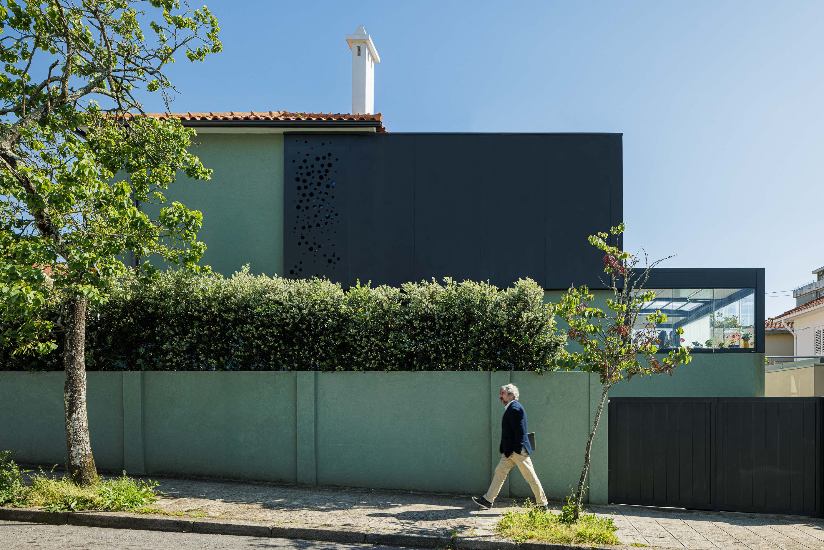 Exterior: Fachada da casa com anexo preto perfurado, marquise envidraçada e jardim. Arquitetura contemporânea. — Casa Pi arquitetura ArquitectosRT em Porto