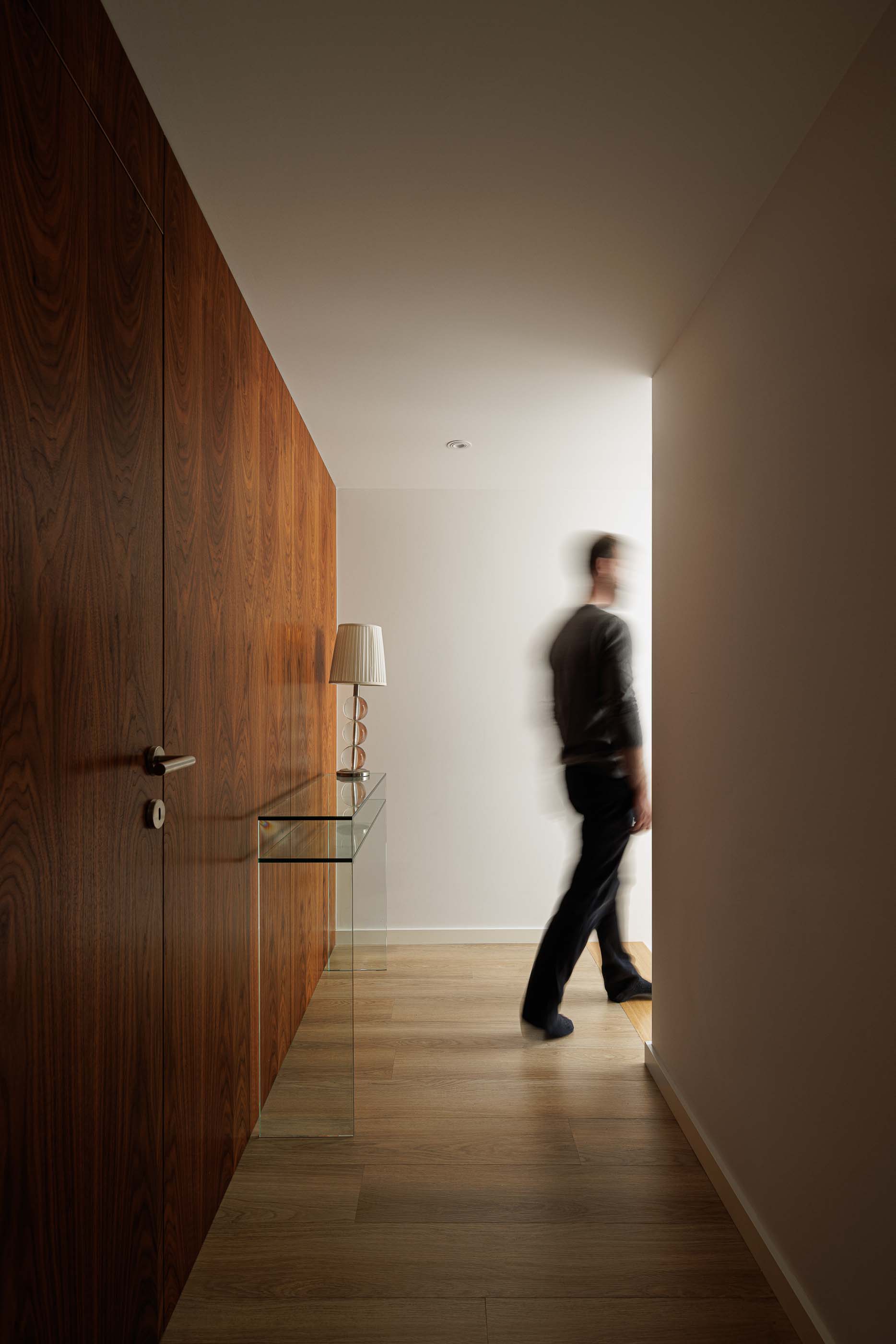 Corredor: Corredor com pavimento em madeira, aparador de vidro e parede revestida a madeira. — Casa Pi arquitetura ArquitectosRT em Porto