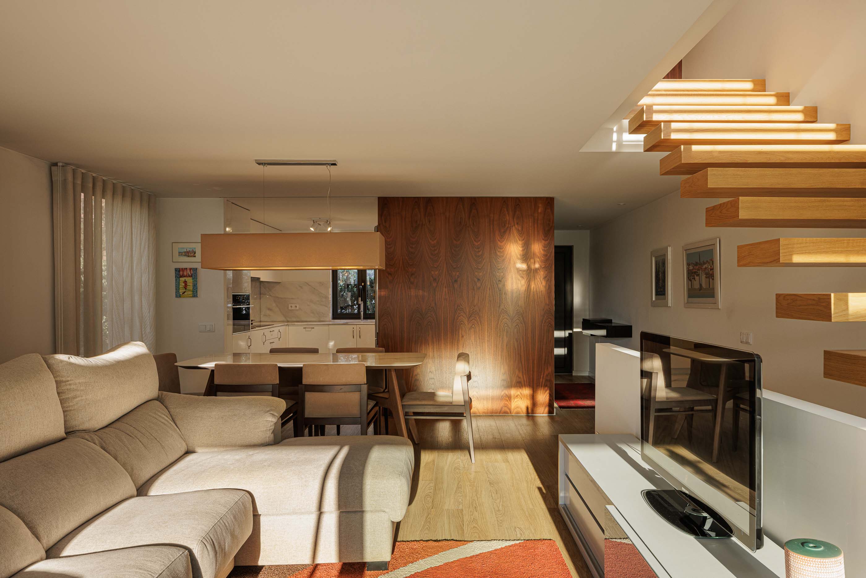Sala de estar/Jantar: Vista da sala de estar com escadas flutuantes, mesa de jantar e cozinha ao fundo. — Casa Pi arquitetura ArquitectosRT em Porto