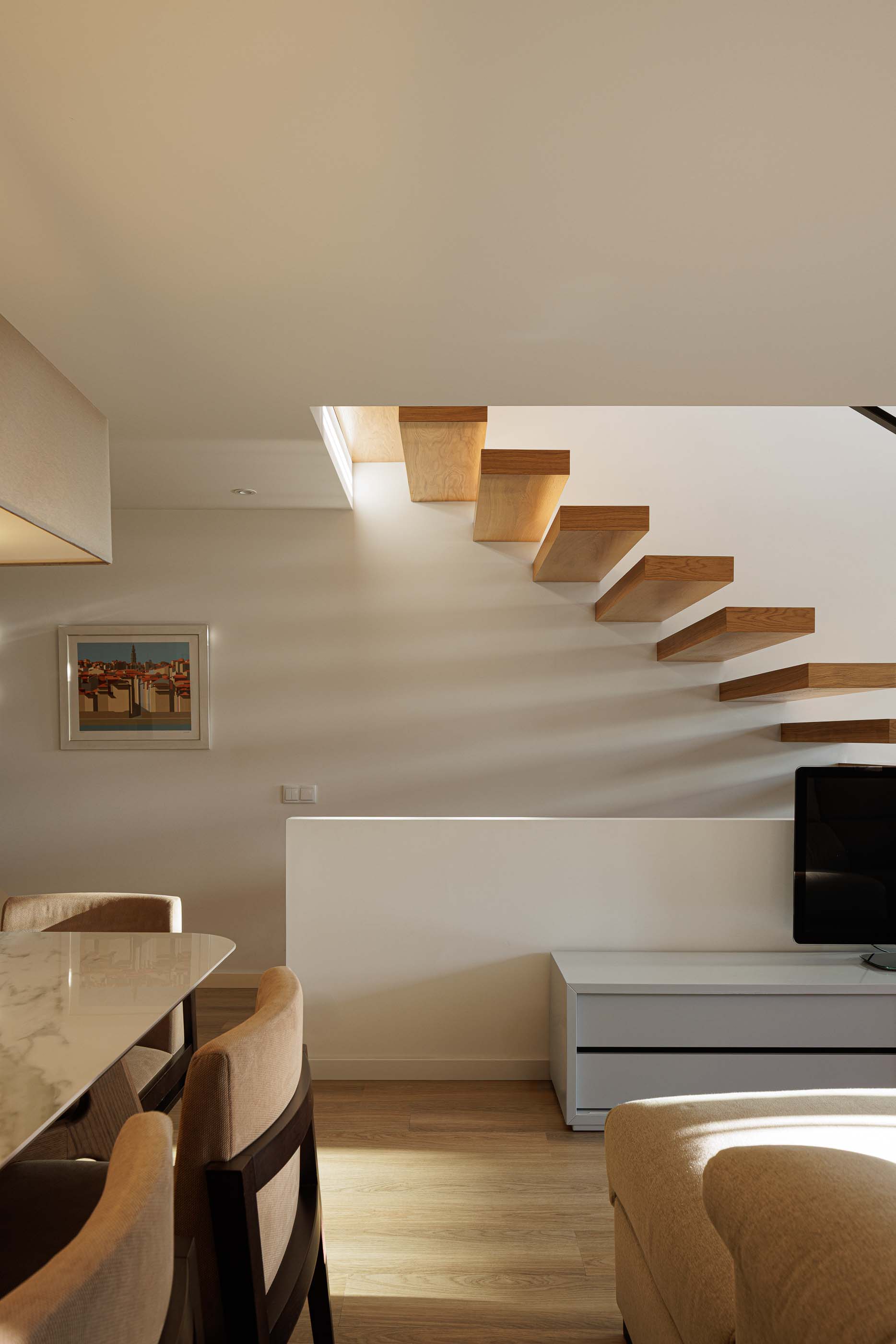 Sala de estar/Jantar: Detalhe da sala de estar com escadas flutuantes, mesa de jantar e móvel de televisão. — Casa Pi arquitetura ArquitectosRT em Porto